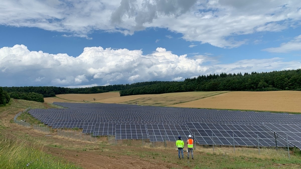 Zwei Arbeiter in Warnwesten stehen vor einem Solarpark auf einem Feld.