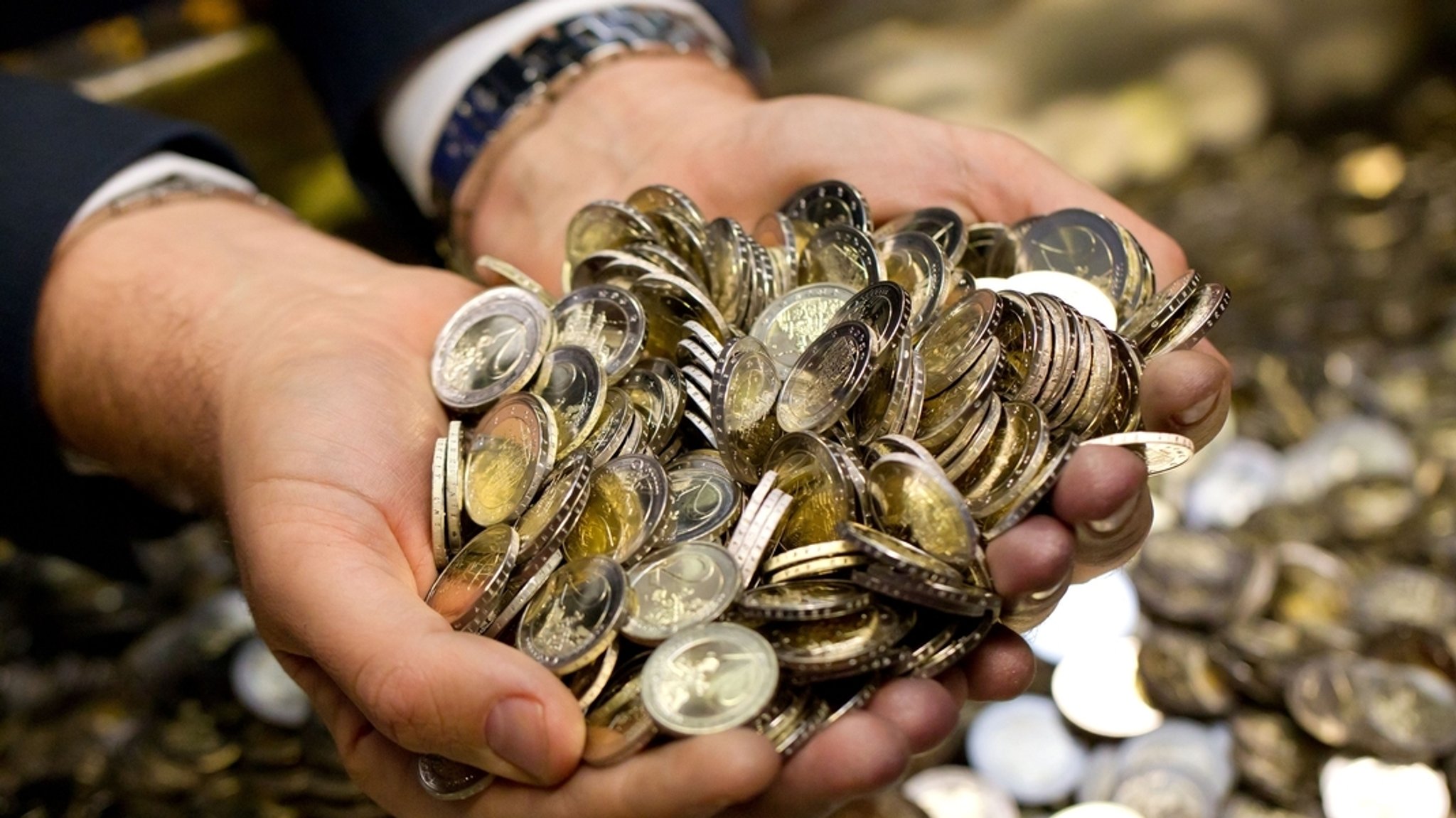 Ein Mann greift mit beiden Händen in einen Hafen Euromünzen