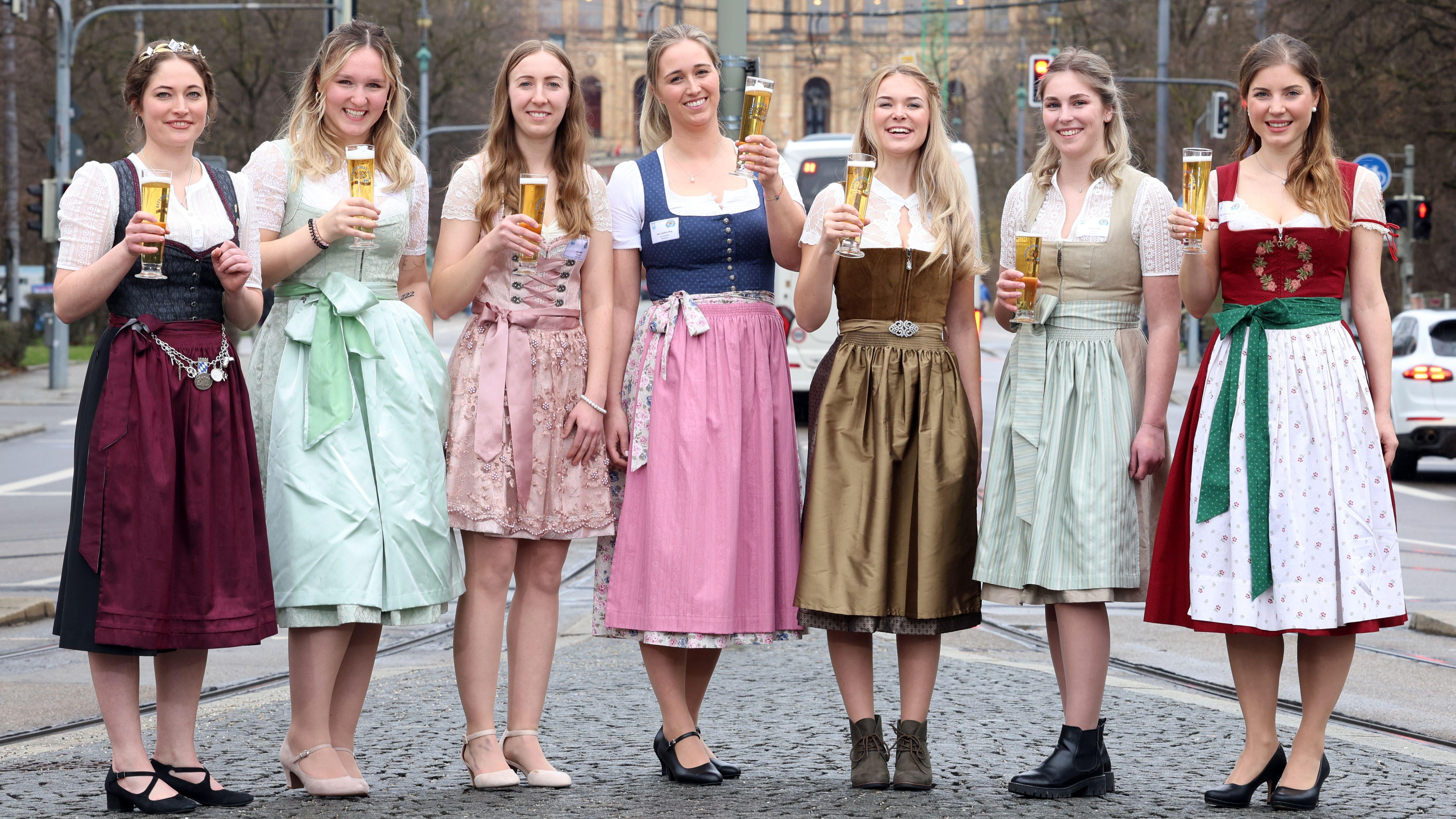 Sieben junge Frauen im Dirndl mit einem Glas Bier in der Hand stehen auf der Straße. 