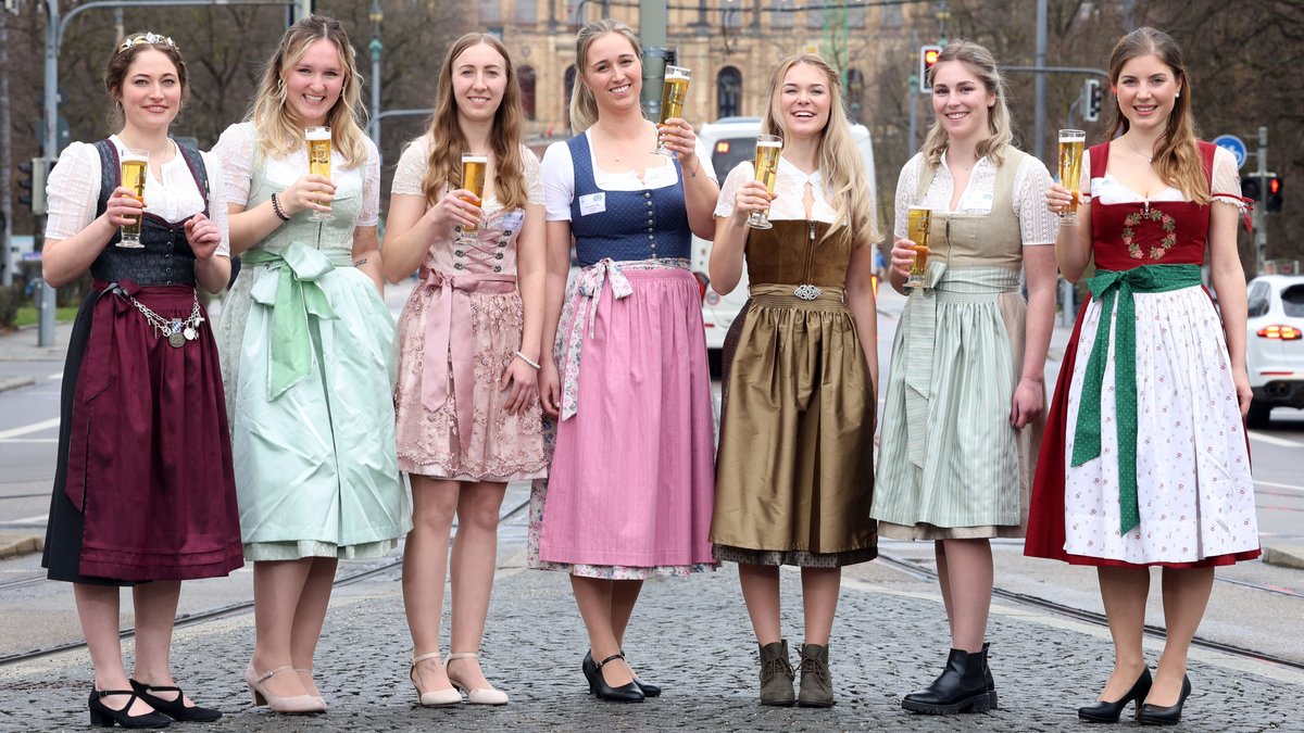 Sieben junge Frauen im Dirndl mit einem Glas Bier in der Hand stehen auf der Straße. 
