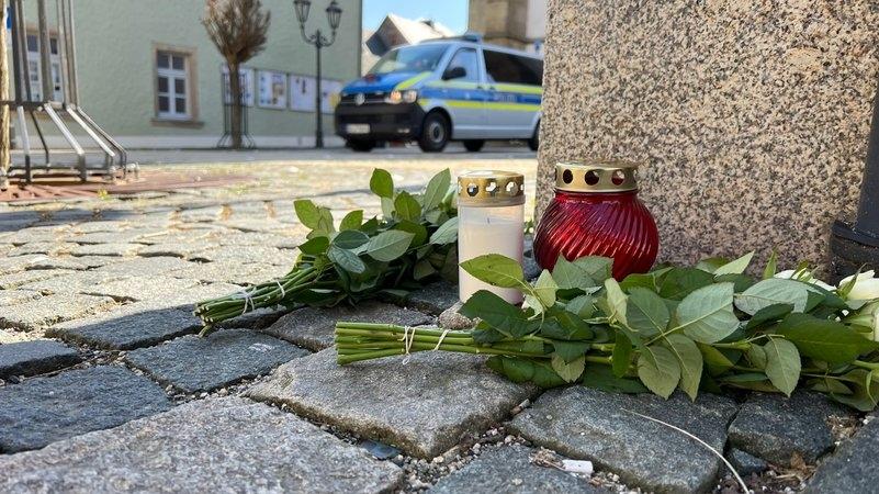 Blumen und Grabkerzen liegen auf dem Boden. 