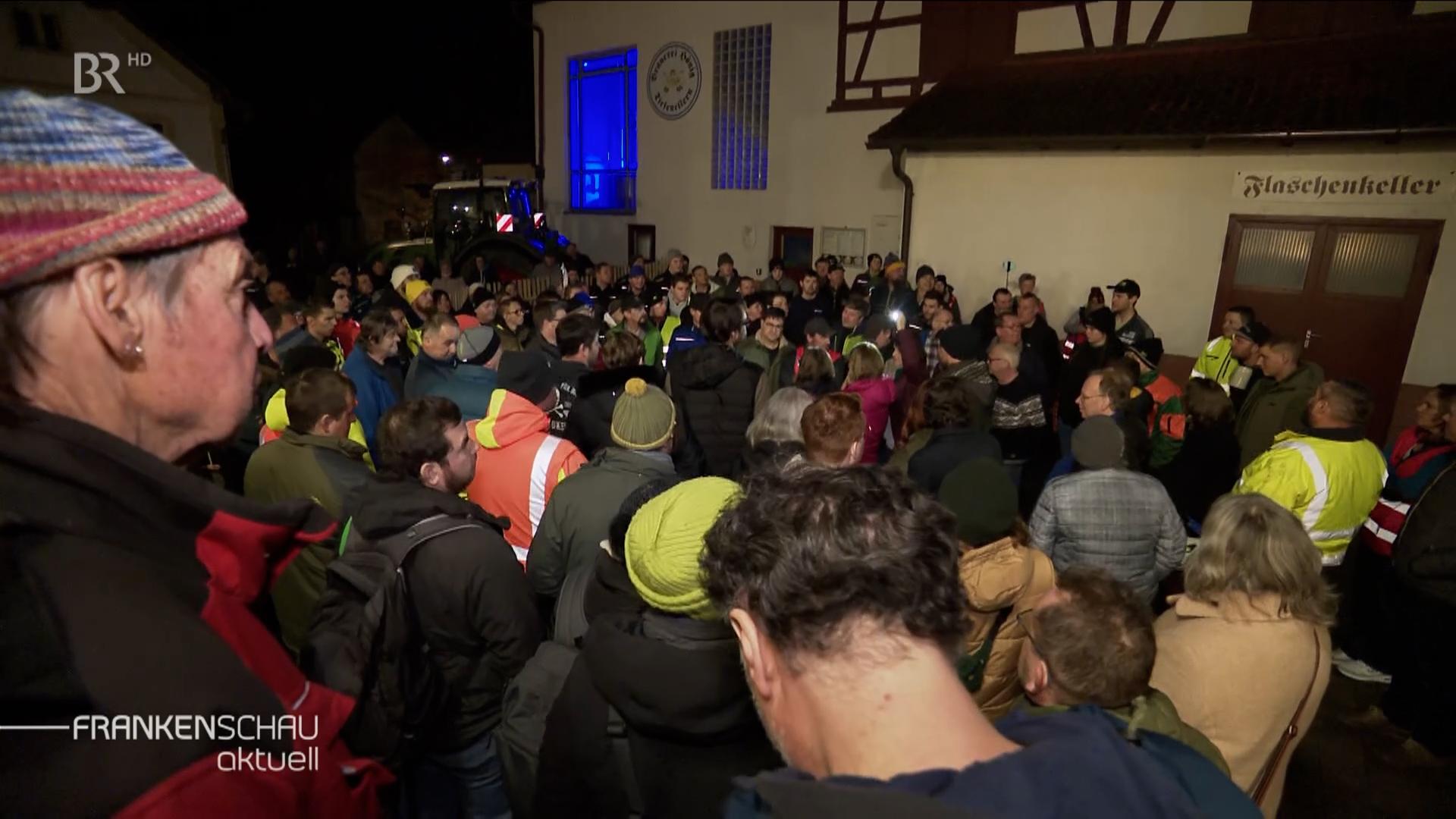 Eine große Menschenansammlung steht vor einem Wirtshaus. 