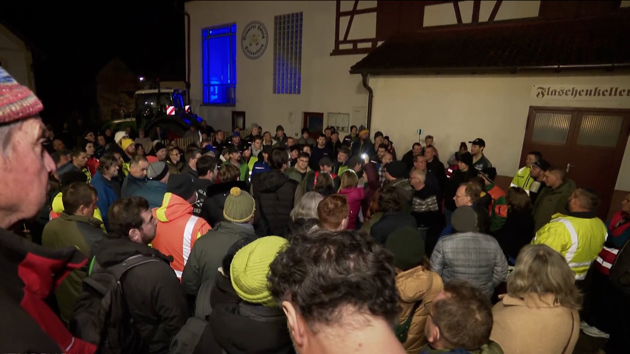 Eine große Menschenansammlung steht vor einem Wirtshaus. 