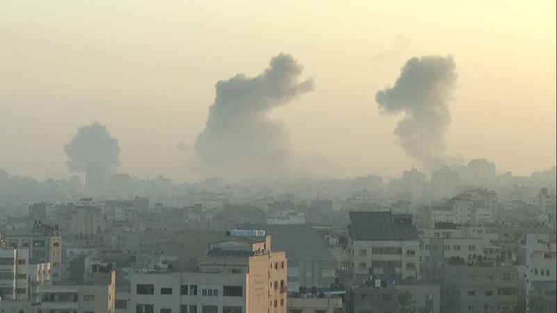 Zerstörte Häuser im Gazastreifen, im Hintergrund Rauchwolken.