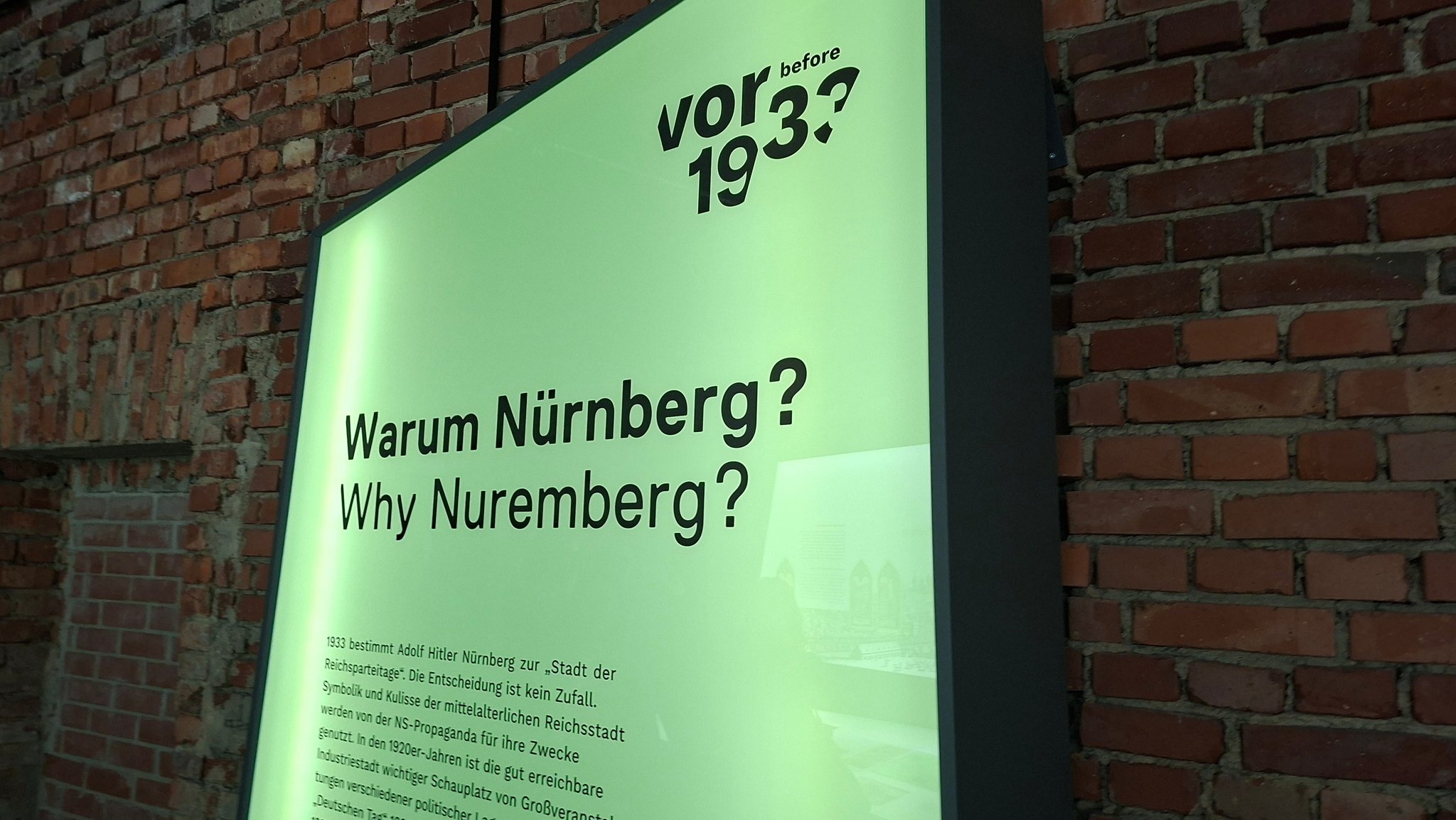 Grüne Ausstellungswand mit der Aufschrift "Warum Nürnberg?". Sie steht vor einer Wand aus roten Ziegeln. Das zeigt den unfertigen Charakter der von Hitler geplanten Kongresshalle. | Bild: BR/Eleonore Birkenstock Grüne Ausstellungswand mit der Aufschrift "Warum Nürnberg?". Sie steht vor einer Wand aus roten Ziegeln. Das zeigt den unfertigen Charakter der von Hitler geplanten Kongresshalle.