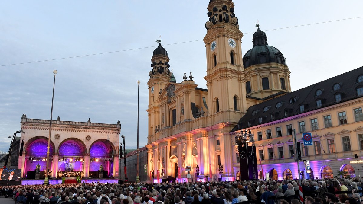 Besucher des Konzerts "Klassik am Odeonsplatz" sitzen auf dem Odeonsplatz, umrahmt von der Feldherrnhalle und der Theatinerkirche. 