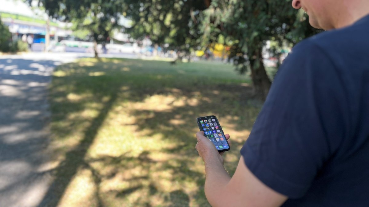 Ein Mann hält in einem Park ein Iphone in der Hand (Symbolbild).