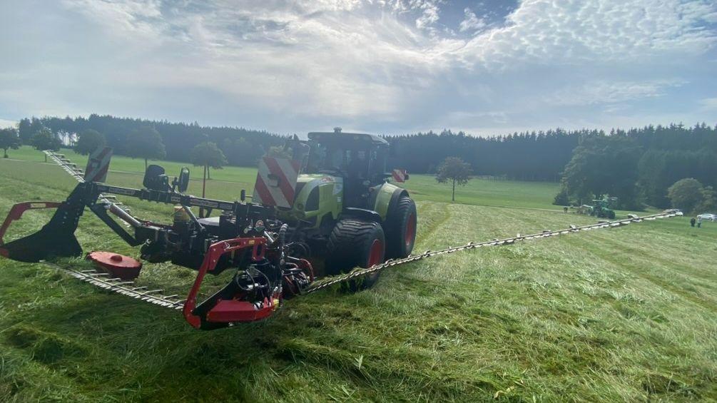Traktor mit Doppelmesser-Technik im Gegenlicht auf einer Wiese im Unterallgäu