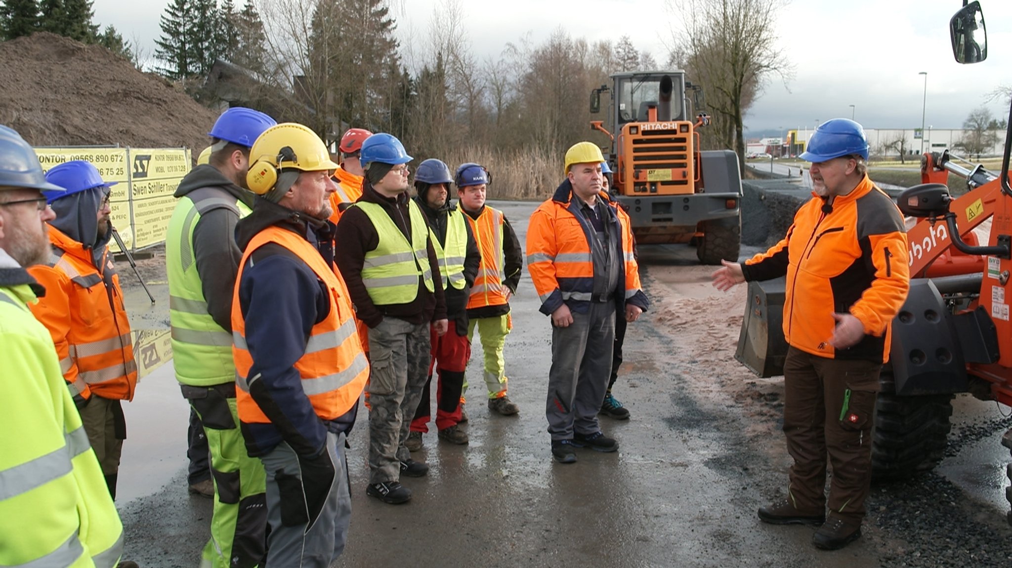 Männer in Warnwesten stehen vor Baumaschinen.