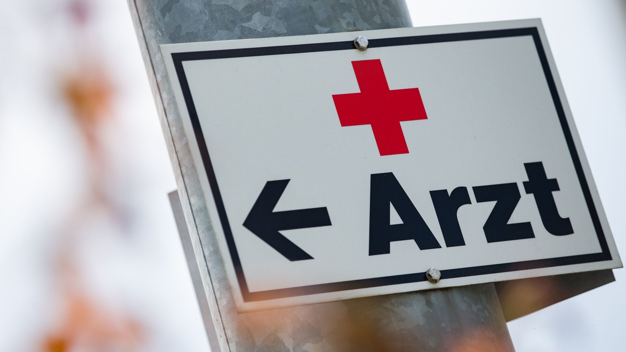 (Symbolbild) Ein Schild mit der Aufschrift "Arzt" hängt an einer Straßenlaterne. 