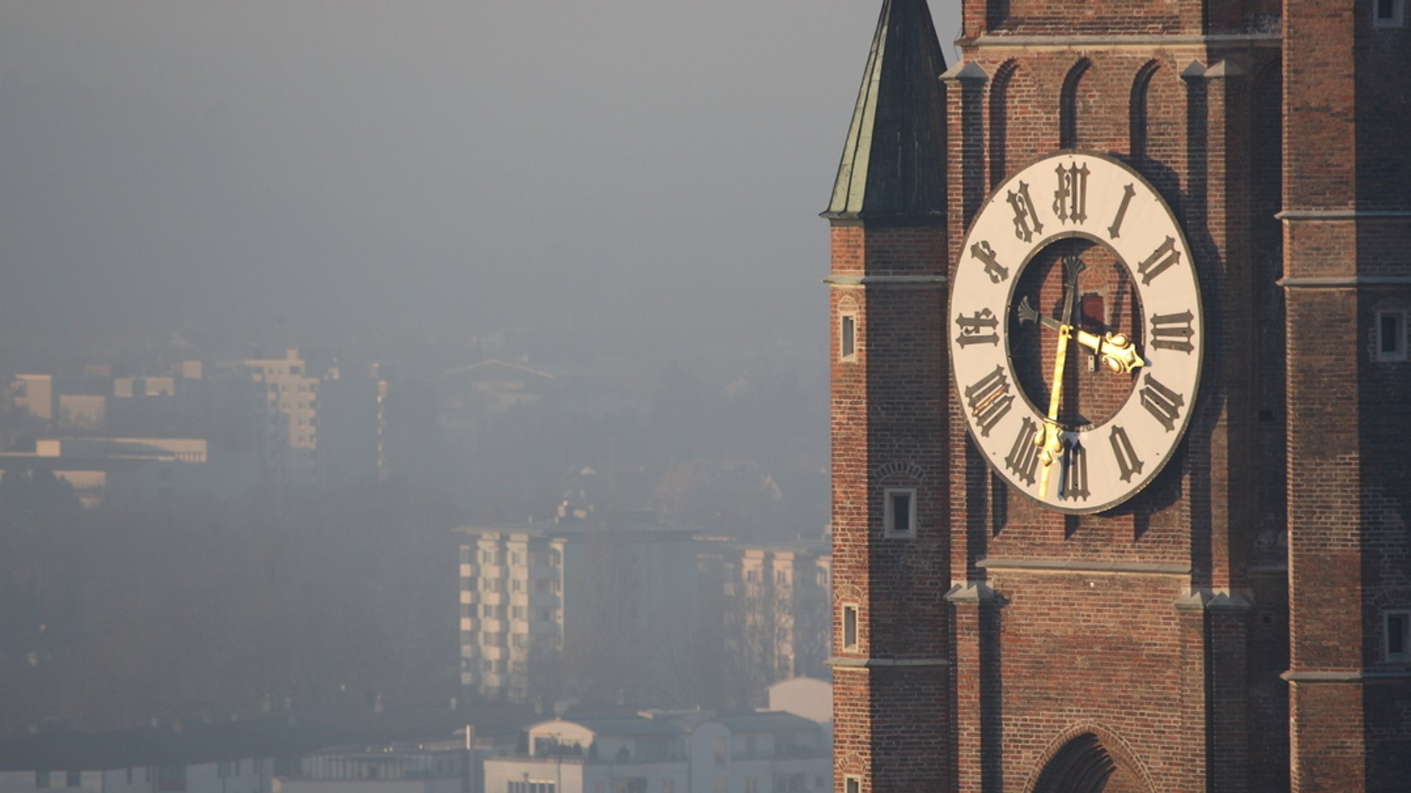 Die Turmuhr der Martinskirche in Landshut, im Hintergrund sind Wohnblöcke zu sehen