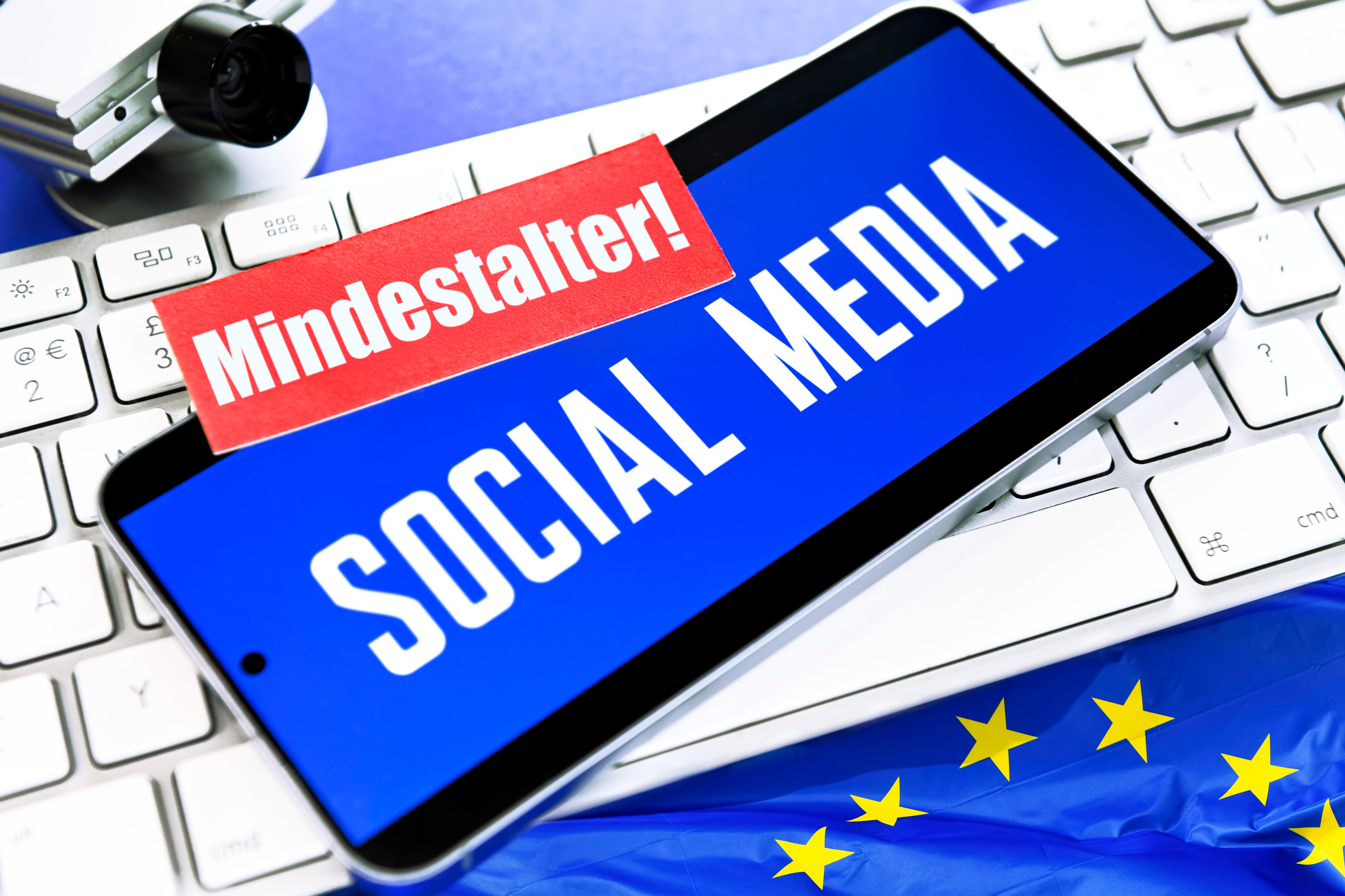 Symbolbild/Fotomontage: Smartphone mit Aufschrift Social Media und Zettel mit Aufschrift "Mindestalter".