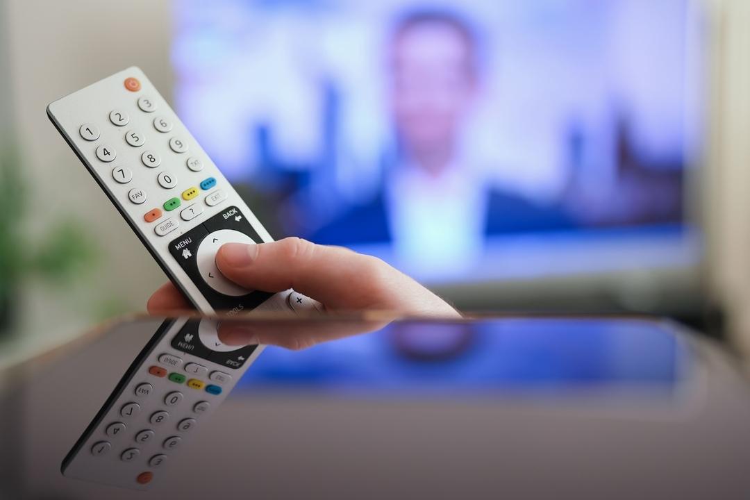 Ein Mann drückt einen Knopf auf der Fernbedienung seines Fernsehers.