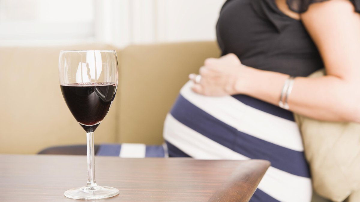 Glas Rotwein auf einem Tisch, schwangere Frau hinten