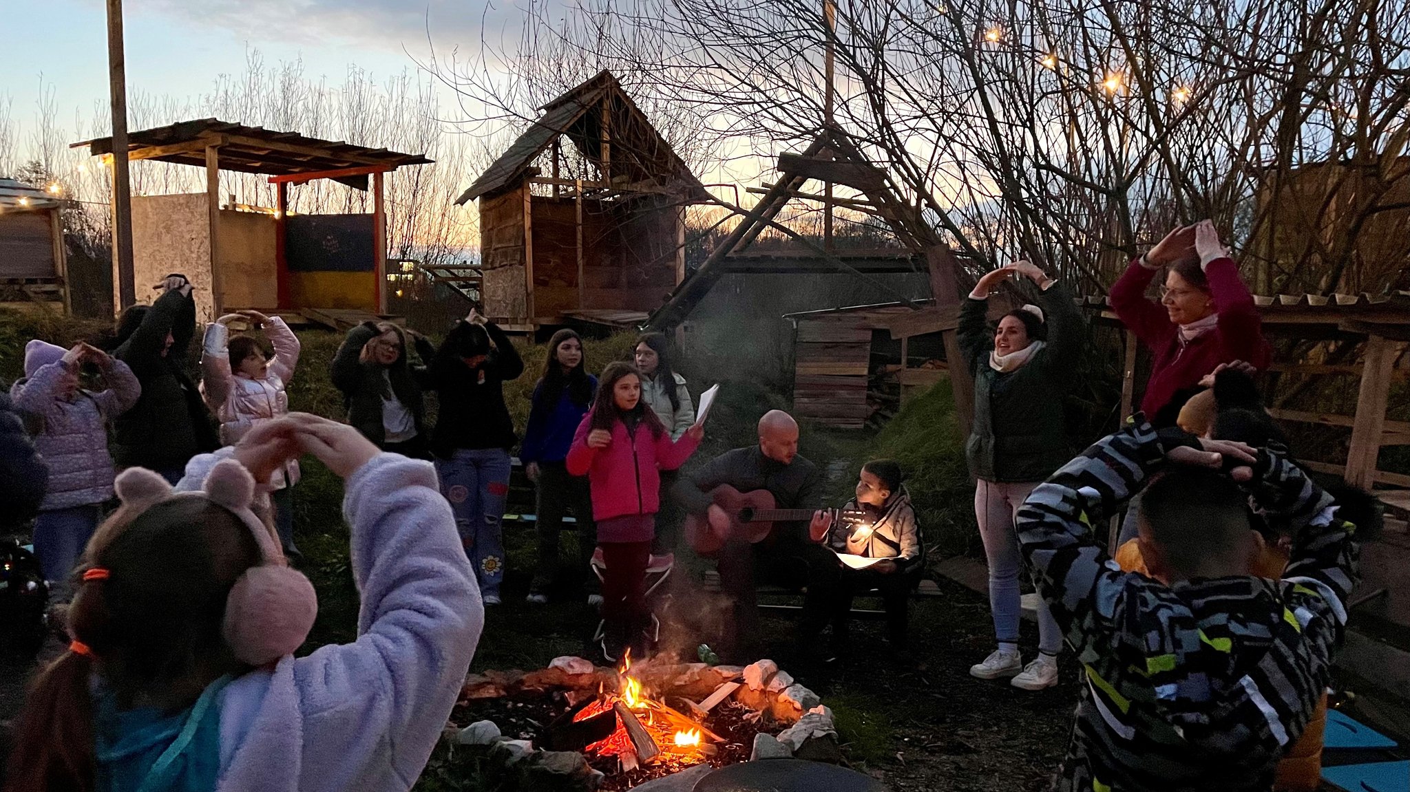 Kinder singen an einem Lagerfeuer.