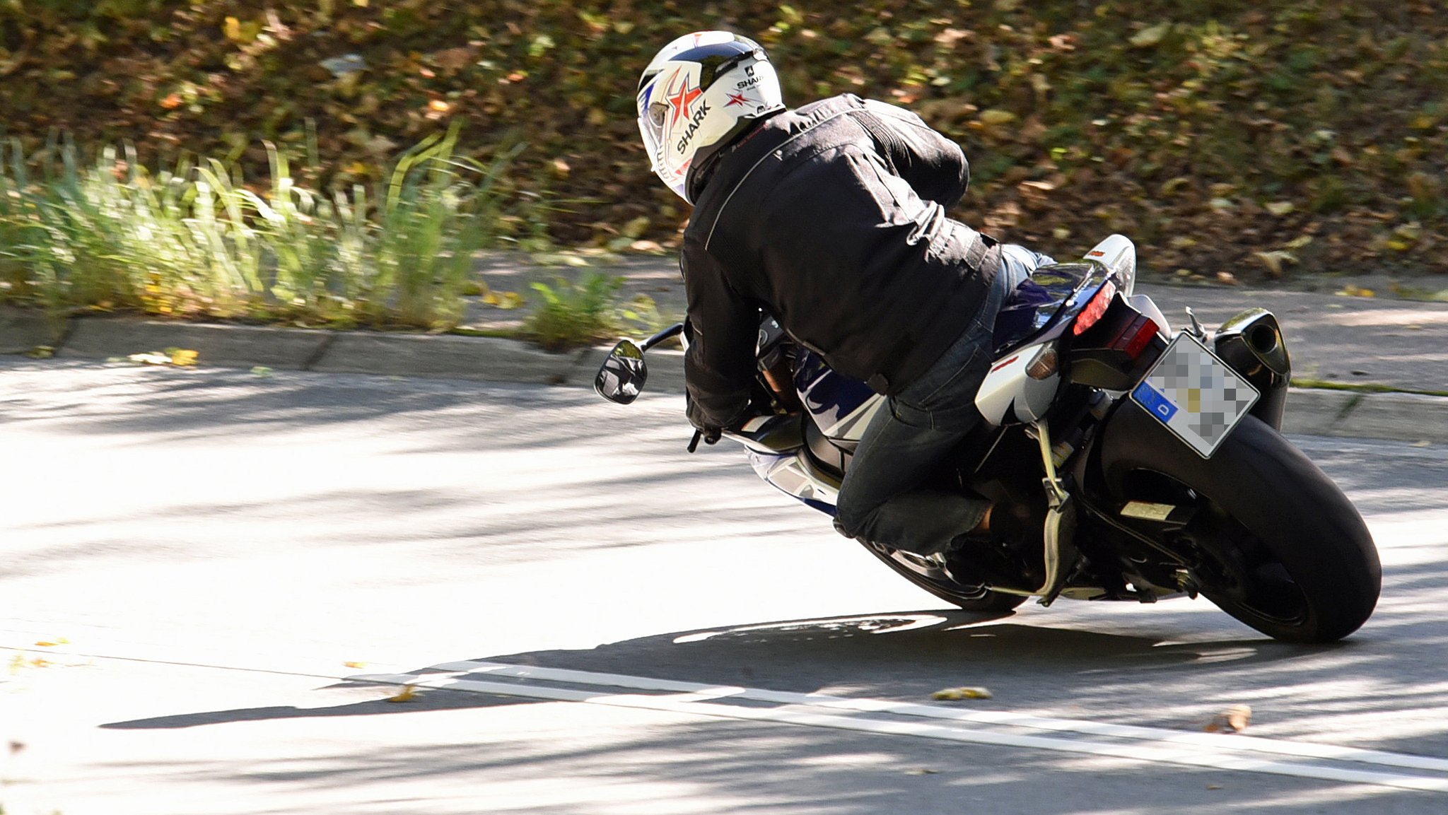 Motorradfahrer von hinten fährt auf einer Landstraße in die Kurve.