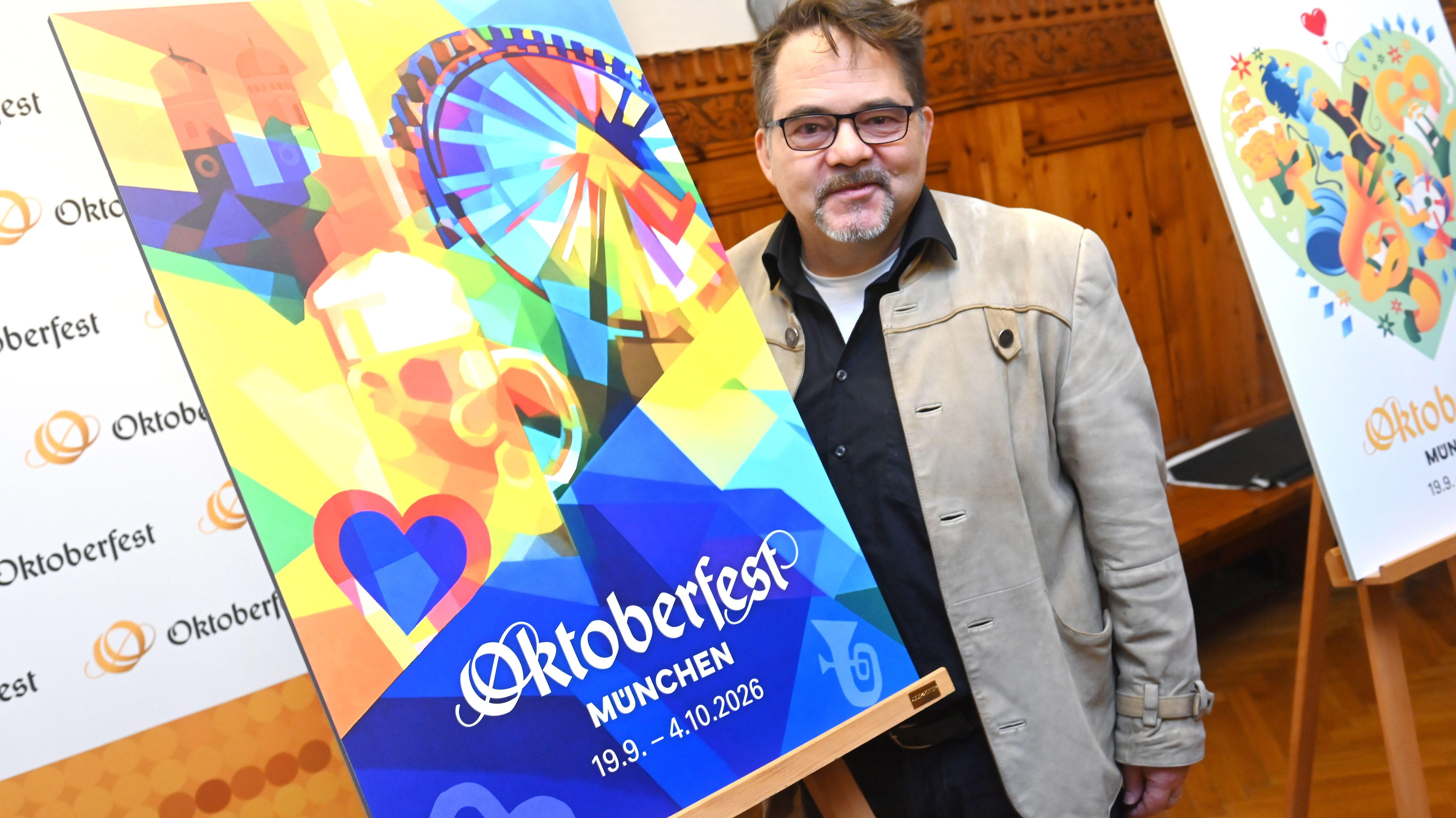 Ein Mann mit Trachtenjanker und Brille hinter seinem Siegesentwurf: Riesenrad, Frauenkirche, Mass Bier in gelb, blau, rot , grün 