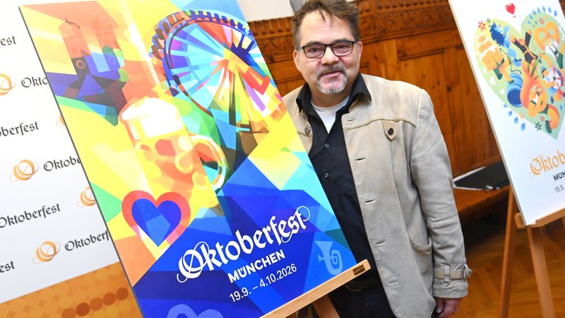 Ein Mann mit Trachtenjanker und Brille hinter seinem Siegesentwurf: Riesenrad, Frauenkirche, Mass Bier in gelb, blau, rot , grün | Bild: picture alliance / SZ Photo | Robert Haas Ein Mann mit Trachtenjanker und Brille hinter seinem Siegesentwurf: Riesenrad, Frauenkirche, Mass Bier in gelb, blau, rot , grün
