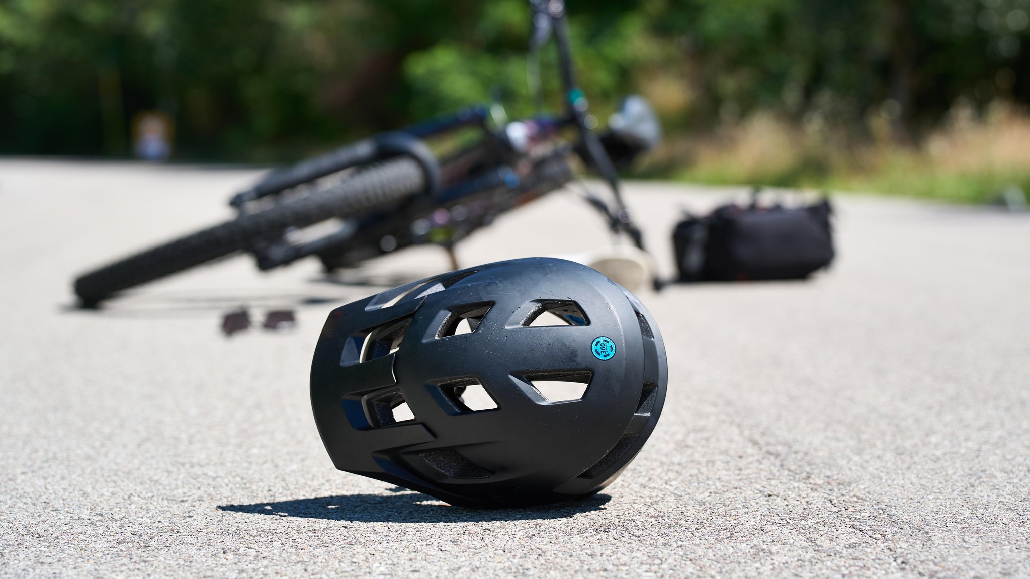 Symbolbild für einen Fahrradunfall: Ein Helm liegt verlassen auf der Straße, im Hintergrund ein gestürztes Fahrrad 