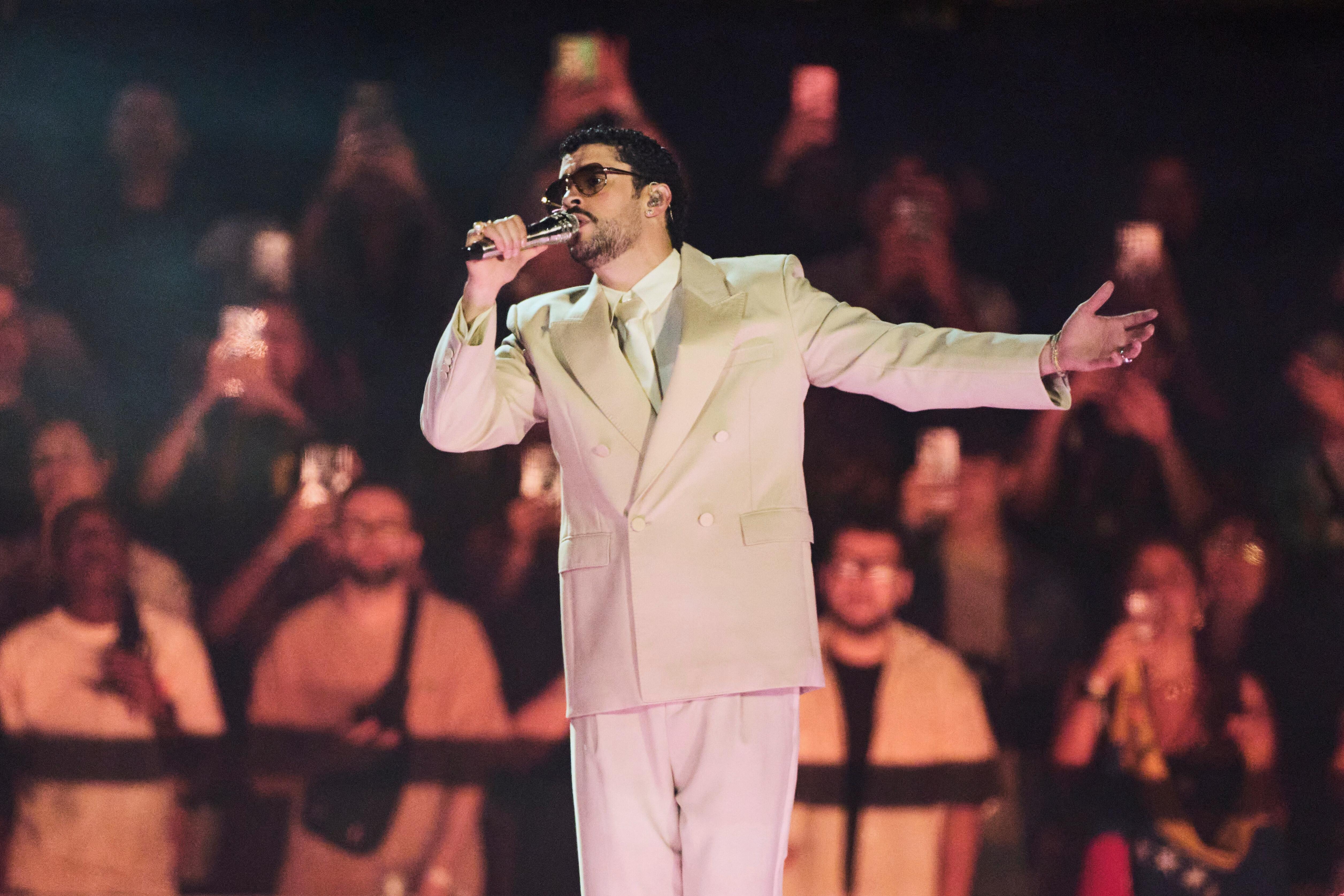 Auf dem Bild ist der Künstler Bad Bunny in einem weißen Anzug, bei seinem Auftritt in Buenos Aires (Argentinien) Anfang Februar zu sehen. Er hält ein Mikrofon in seiner Hand und singt.  | Bild:picture alliance / ASSOCIATED PRESS | Rodrigo Abd
