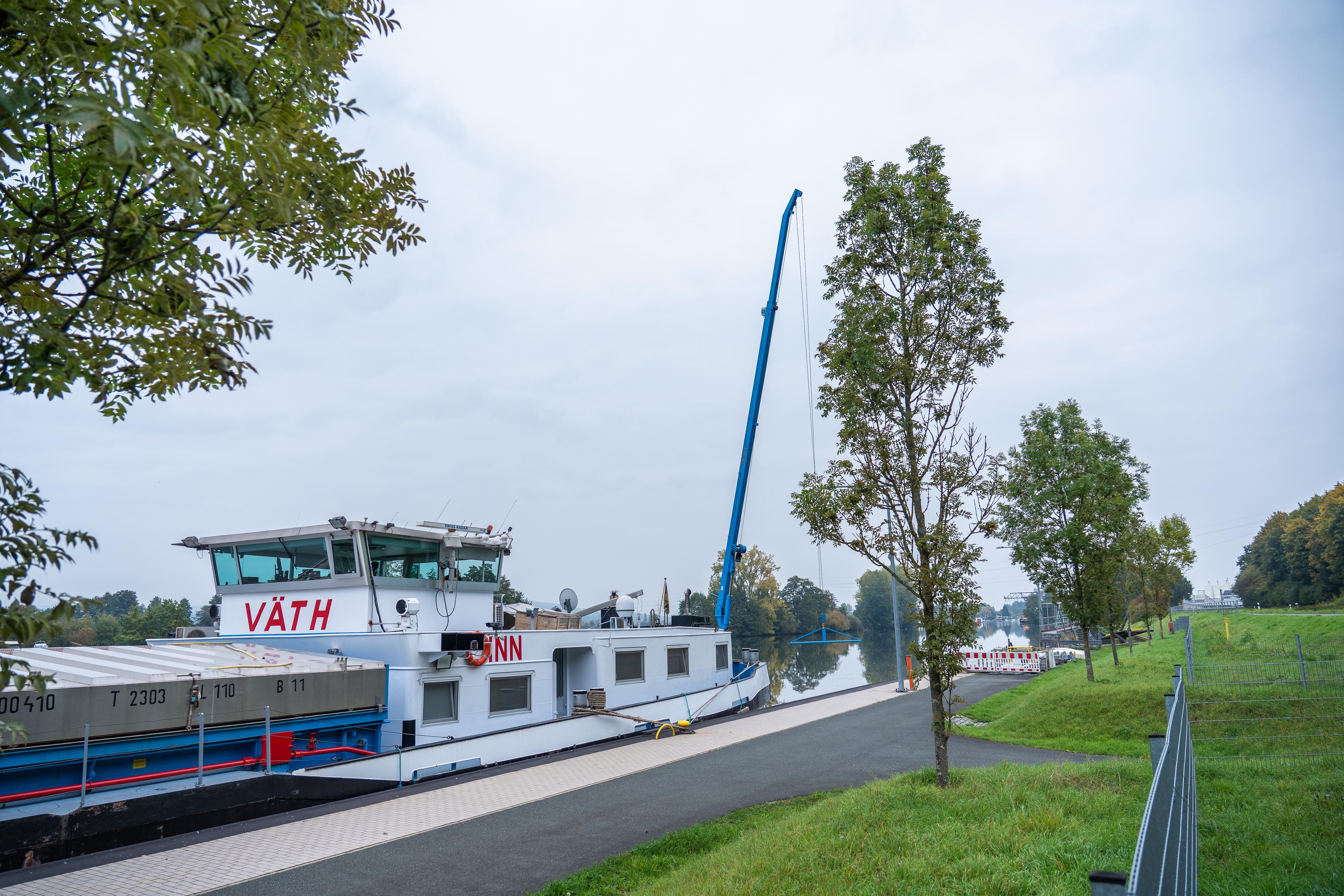 Ein Schiff mit ausgefahrenem Kran steht am Ufer. 