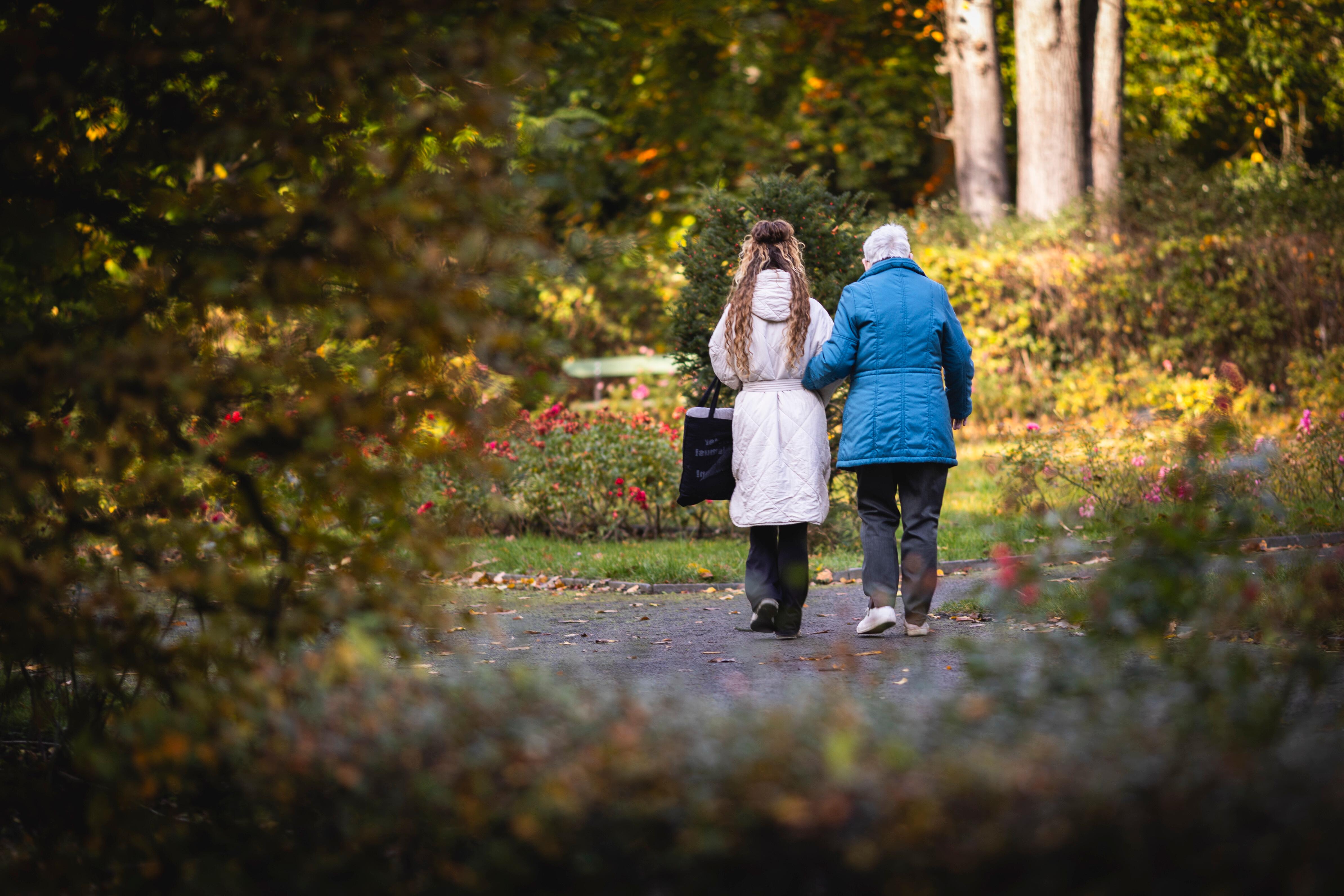 Eine junge Frau und eine Seniorin machen einen morgendlichen Spaziergang durch einen Park.