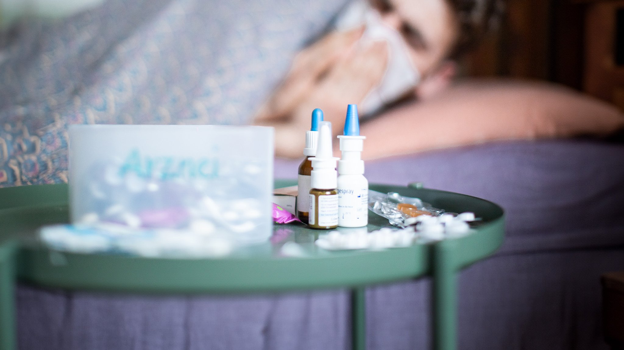 Ein Mann liegt krank im Bett und hat auf dem Nachttisch jede Menge Meidkamente stehen (Symbolbild).