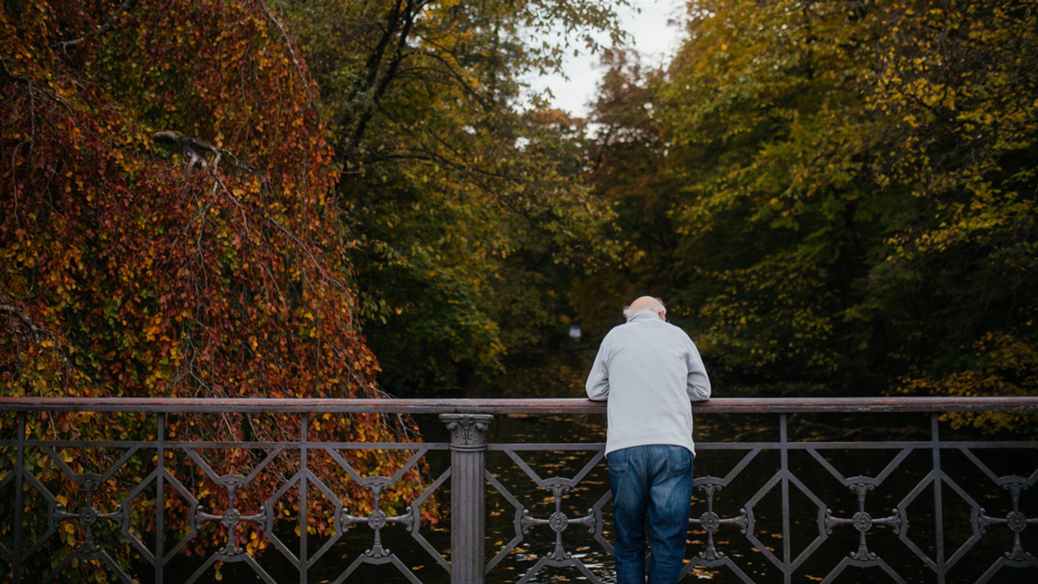 Ein älterer Mann steht auf einer Brücke und Blick ins Wasser.