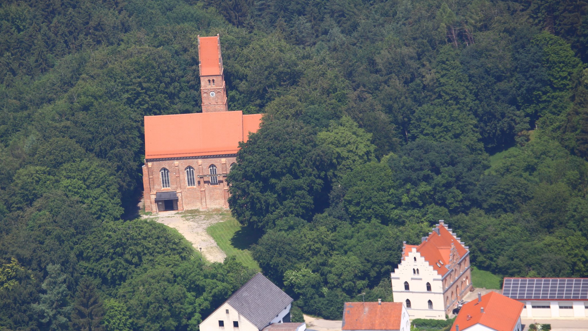 Aus der Luft aufgenommen sieht man die Burgkirche Oberwittelsbach, dahinter Wald.