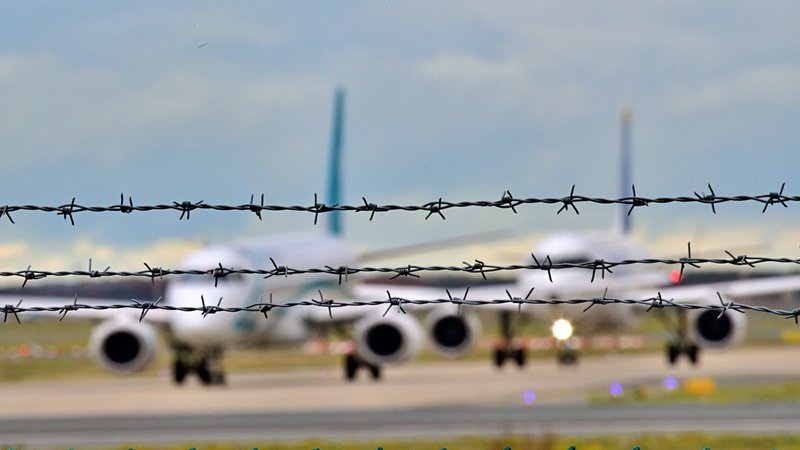 Drei Reihen Stacheldraht, dahinter in Unschärfe zwei Flugzeuge auf der Landebahn. (Symbolbild) Der Bügerkrieg in Syrien ist beendet. Soll in das Land wieder abgeschoben werden? Über diese Frage ist eine Debatte entbrannt. | Bild: picture alliance / Daniel Kubirski Drei Reihen Stacheldraht, dahinter in Unschärfe zwei Flugzeuge auf der Landebahn. (Symbolbild) Der Bügerkrieg in Syrien ist beendet. Soll in das Land wieder abgeschoben werden? Über diese Frage ist eine Debatte entbrannt.