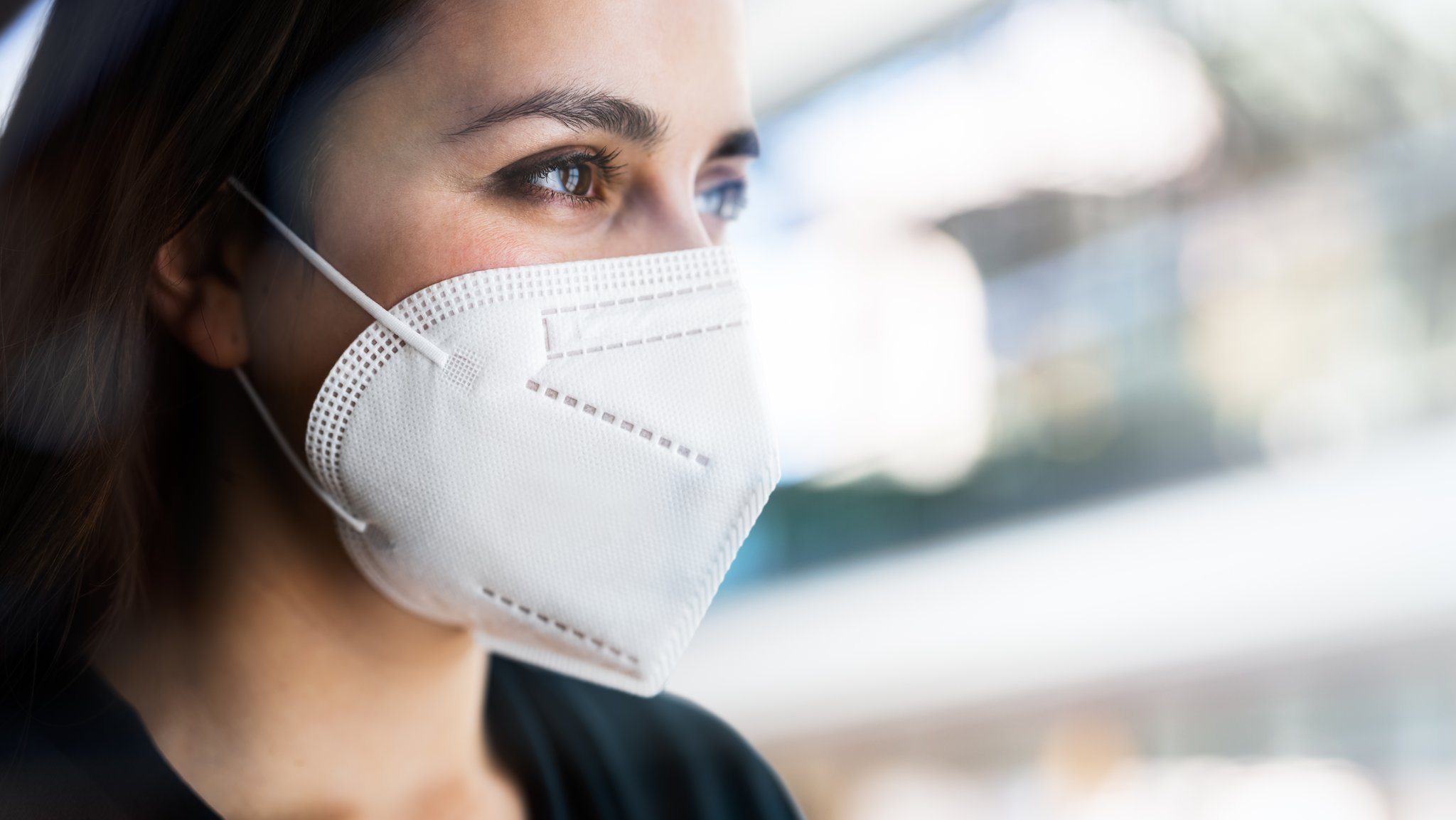 Frau mit FFP2-Maske blickt zum Fenster hinaus