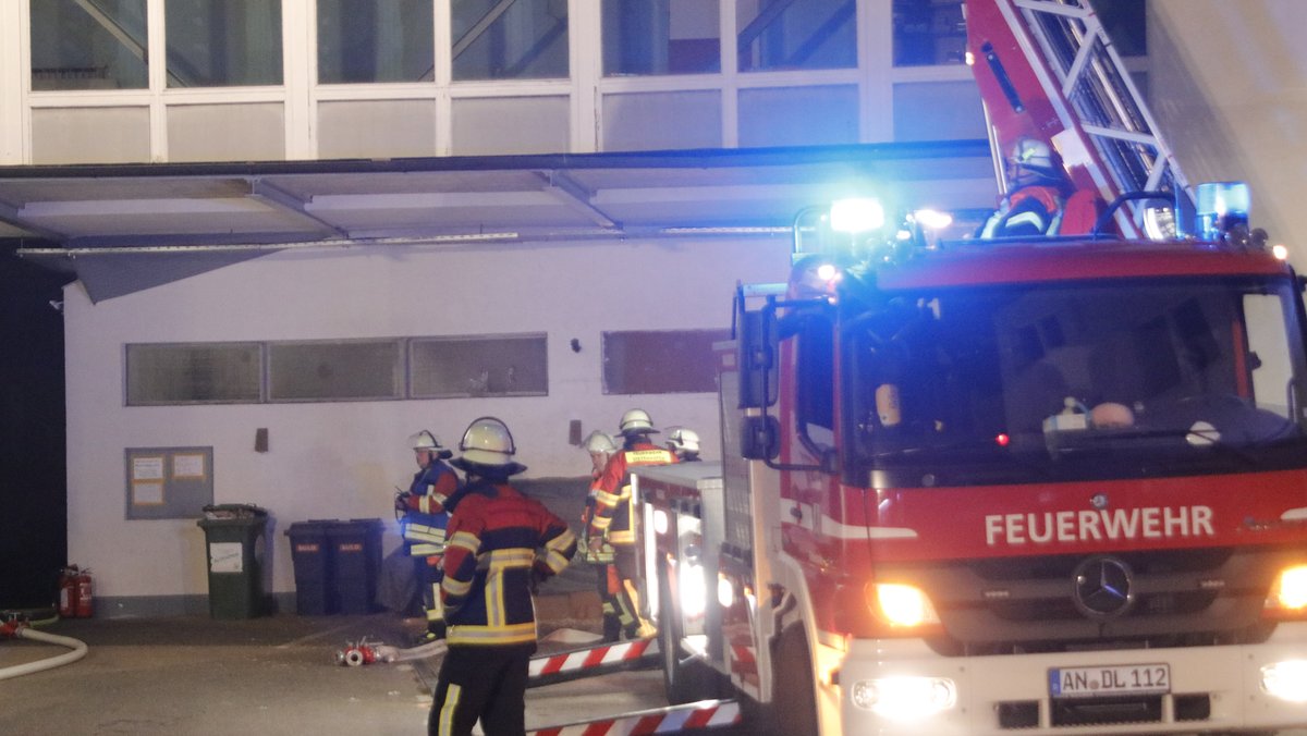 Ein Feuerwehrauto mit ausgefahrener Leiter und Feuerwehrleute vor einem Gebäude.