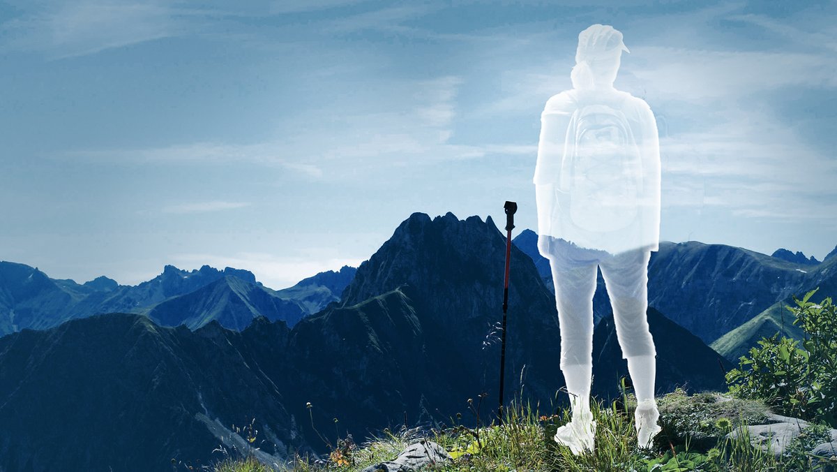 Eine durchsichtige Frau in Wanderkleidung steht auf einem Berg und schaut sich das Panorama an. (Symbolbild)