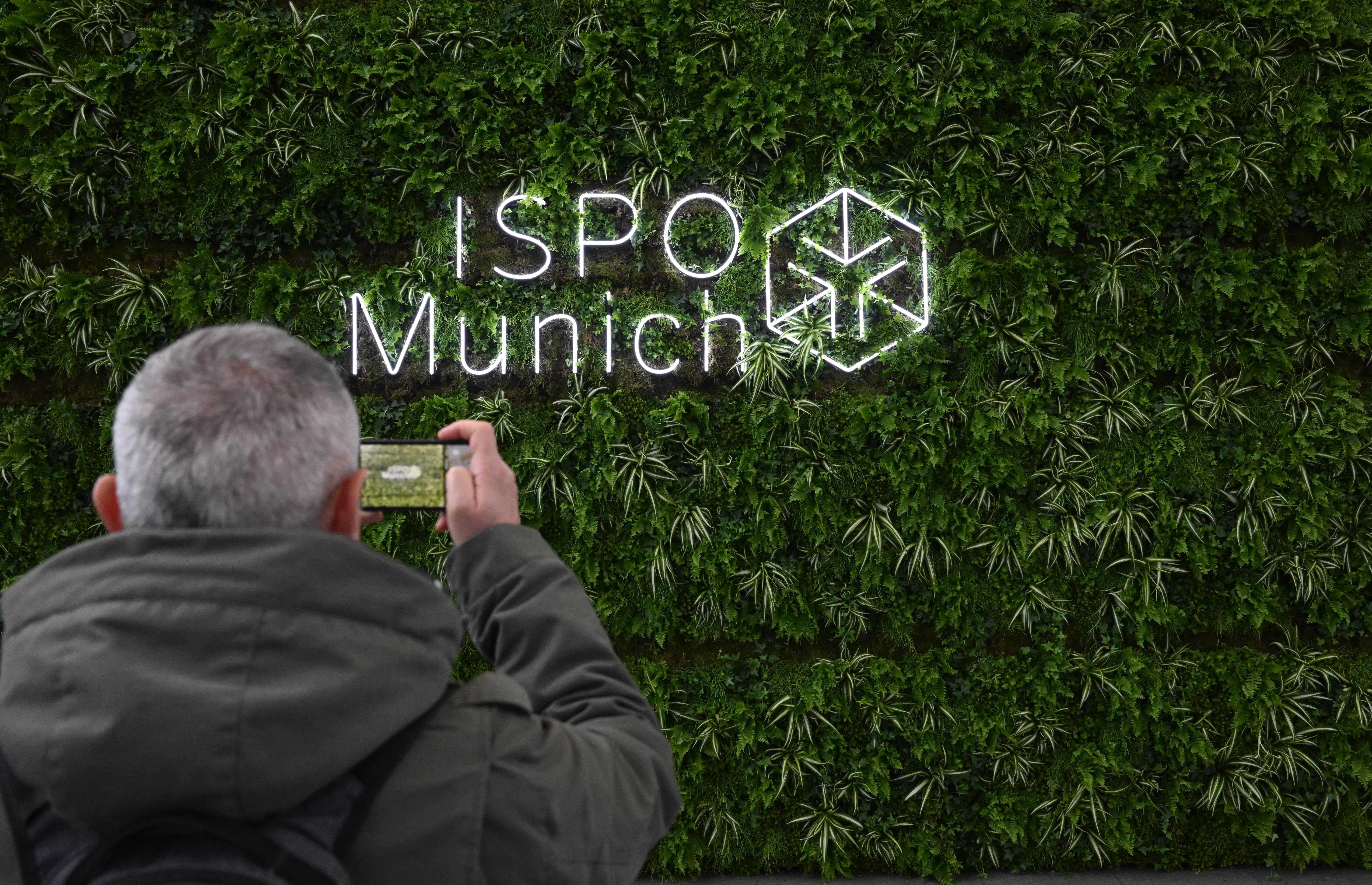 Ein Besucher fotografiert das Logo der Sportartikelmesse Ispo in der Eingangshalle der Messe München.