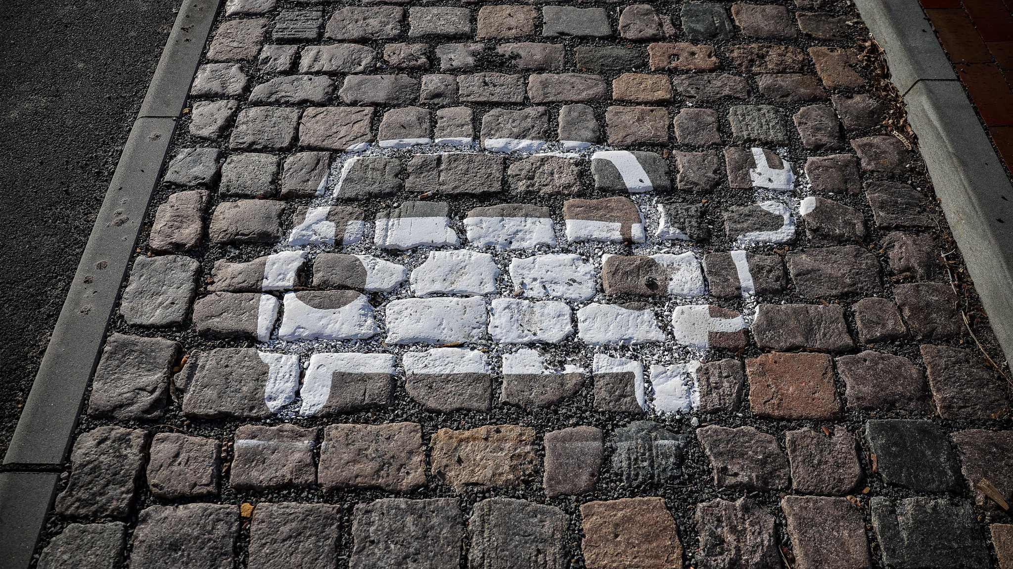 Ein symbolisiertes Auto mit Kabel und Stecker ist auf das Pflaster einer Parkbucht mit Ladesäule gemalt.