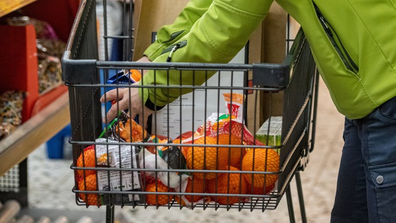 Eine Frau legt in einem Supermarkt Lebensmittel in einen Einkaufswagen.