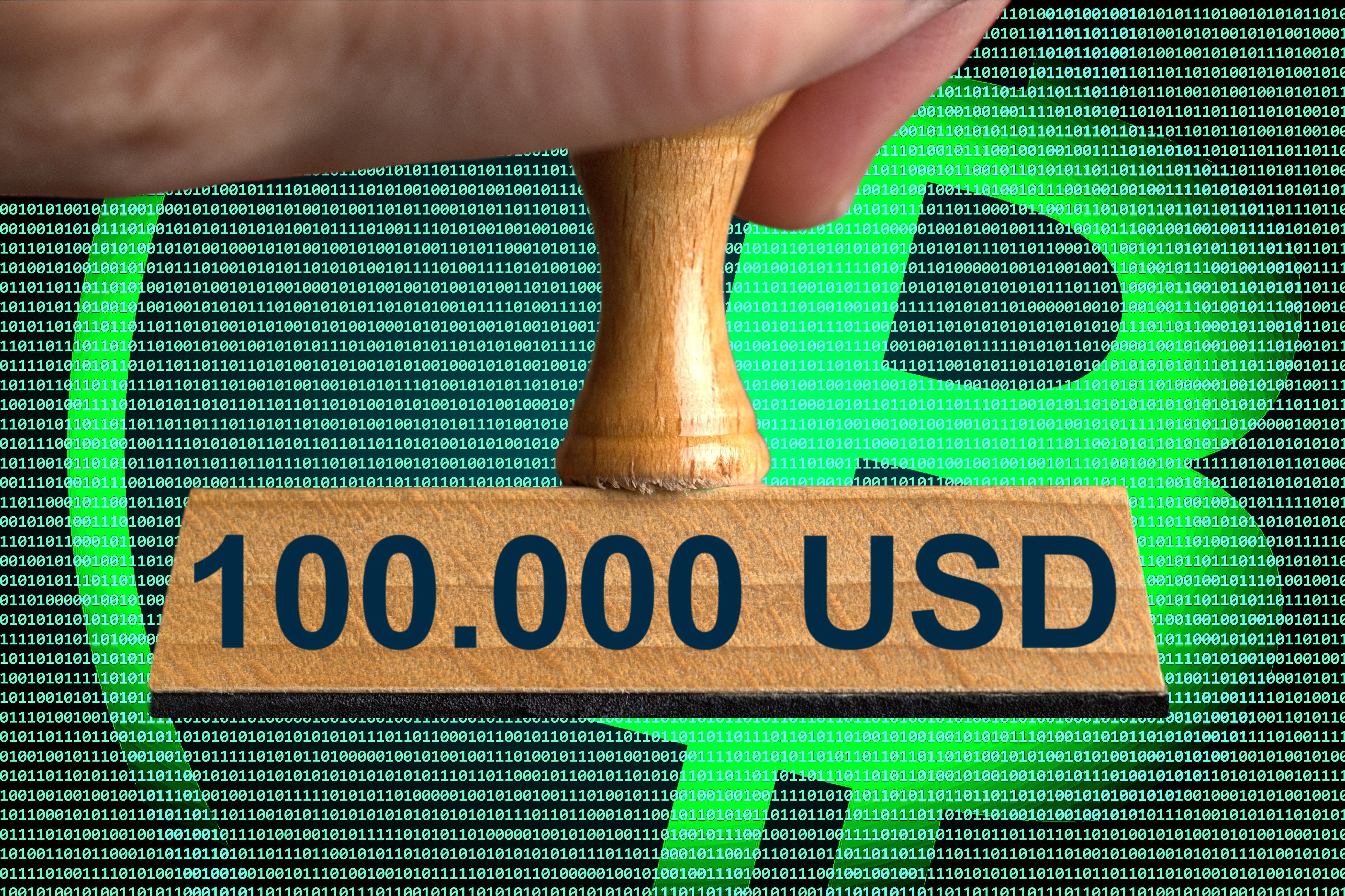 Hand mit einem 100.000-Dollar-Stempel vor Bitcoin-Logo