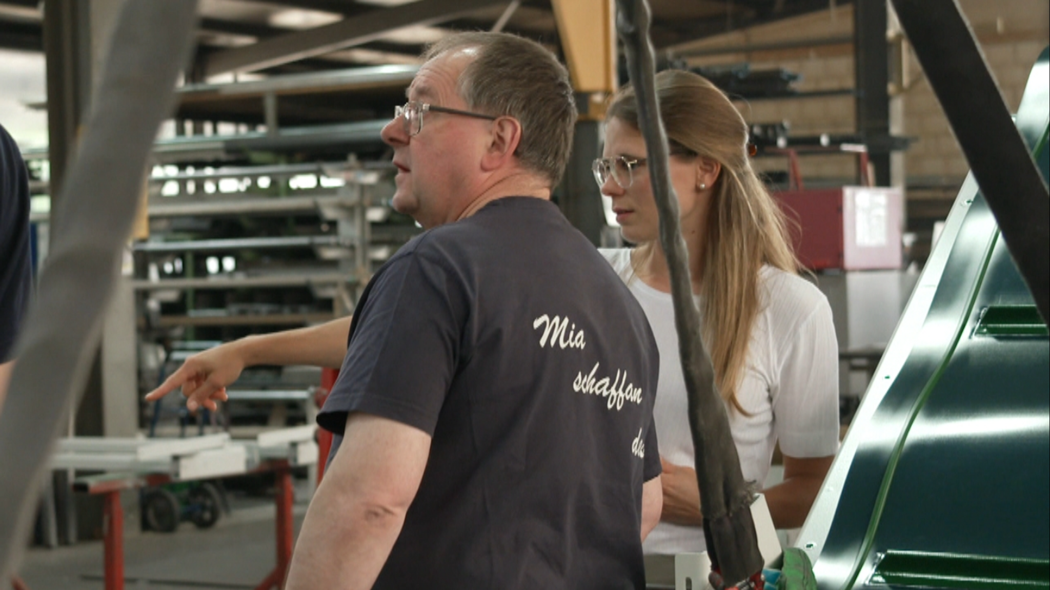 Eine Frau und ein Mann stehen in einer Produktionshalle und besprechen etwas.