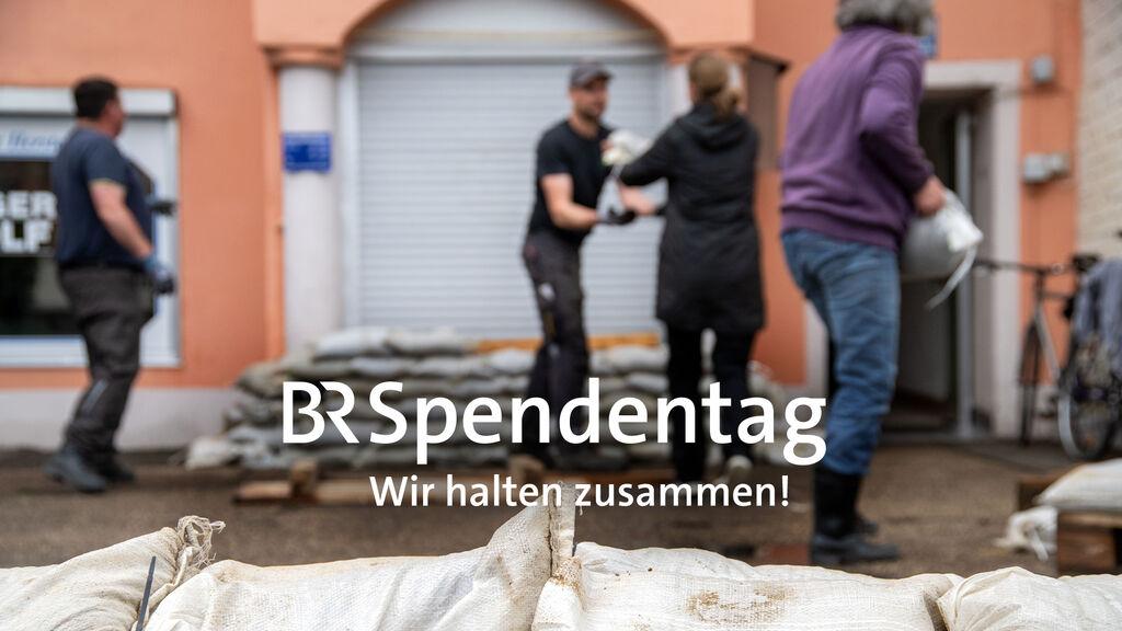 Symbolbild zum "BR Spendentag - Wir halten zusammen!" - Vier Menschen schichten Sandsäcke auf 