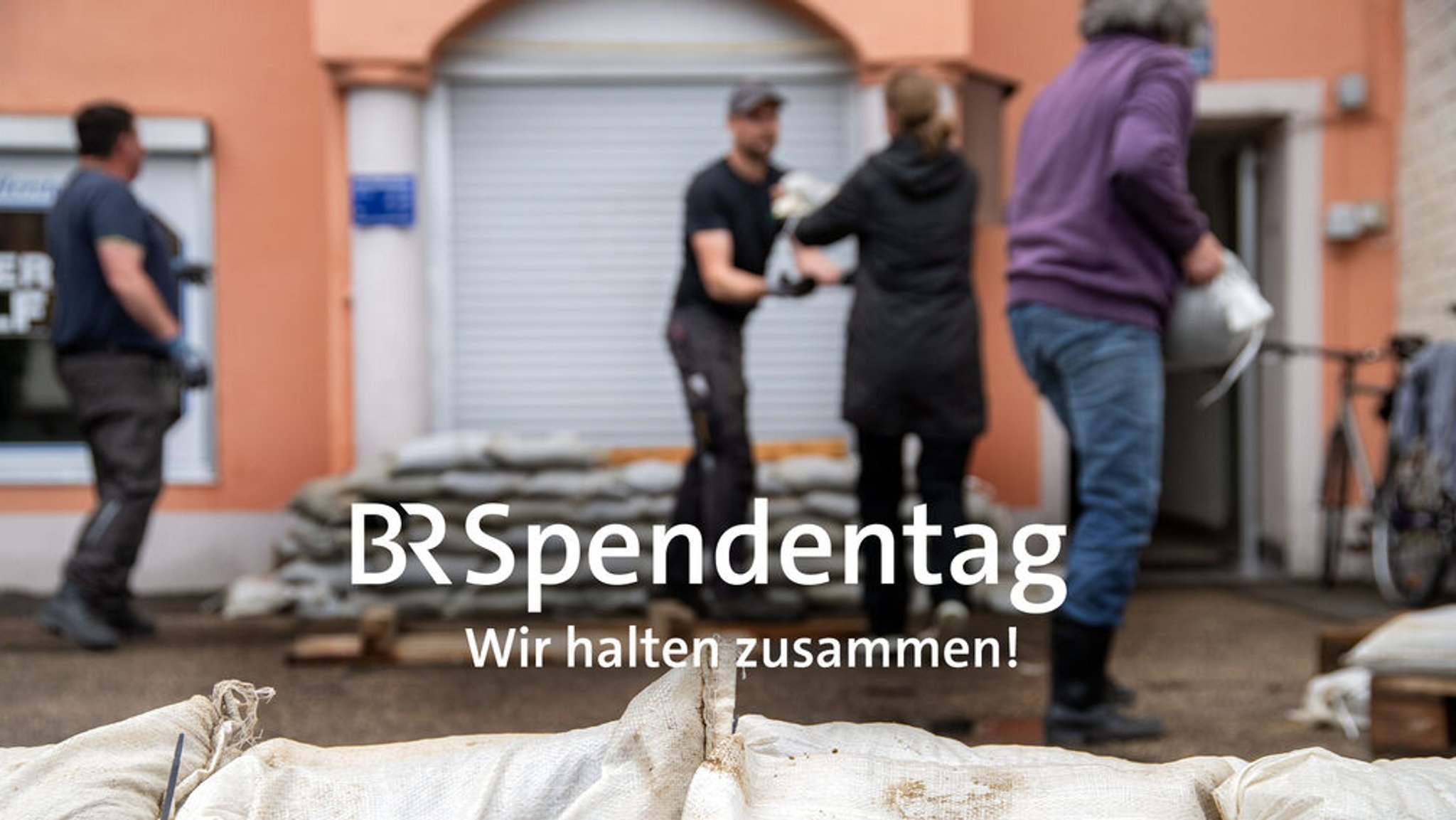 Symbolbild zum "BR Spendentag - Wir halten zusammen!" - Vier Menschen schichten Sandsäcke auf 