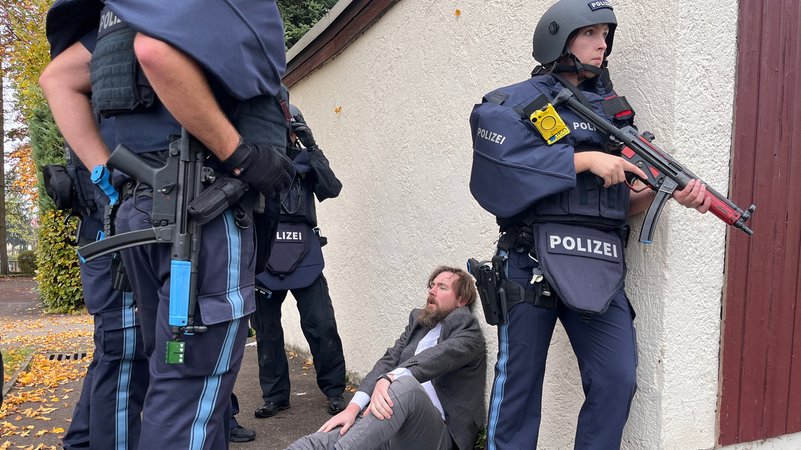 Ein Schauspieler mimt einen Verletzten beim Training für eine Amoklauf in Ichenhausen. Er sitzt an eine Wand gelehnt, umgeben von bewaffneten Polizisten. | Bild: BR/Peter Allgaier Ein Schauspieler mimt einen Verletzten beim Training für eine Amoklauf in Ichenhausen. Er sitzt an eine Wand gelehnt, umgeben von bewaffneten Polizisten.
