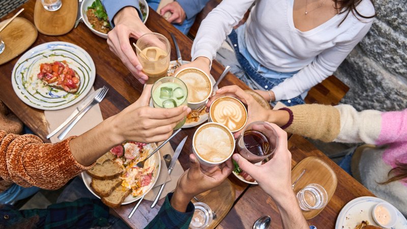 Junge Menschen prosten sich in einem Restaurant zu. | Bild: picture alliance / Westend61 | Oscar Martin Sanchez Junge Menschen prosten sich in einem Restaurant zu.