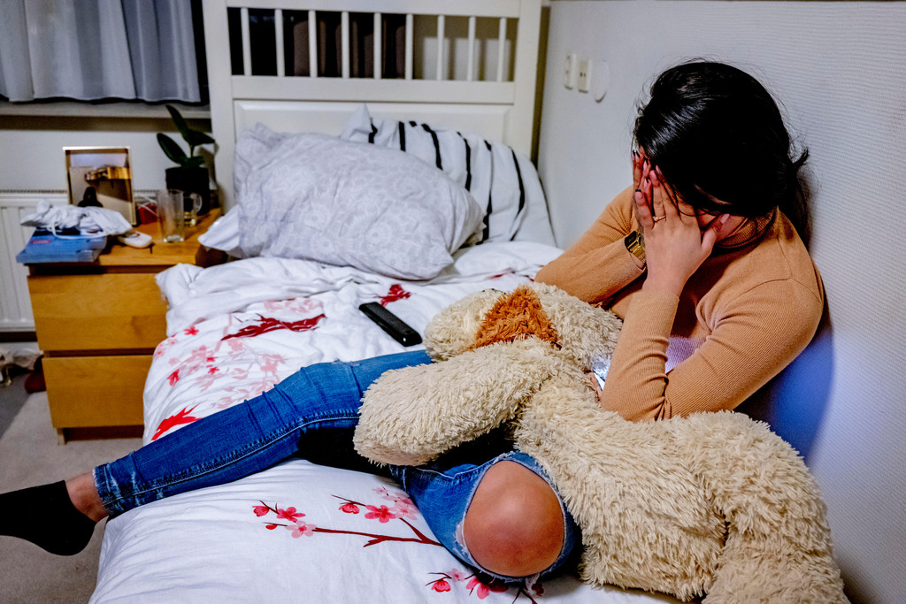 Eine Jugendliche sitzt auf ihrem Bett und hält die Hände vors Gesicht.