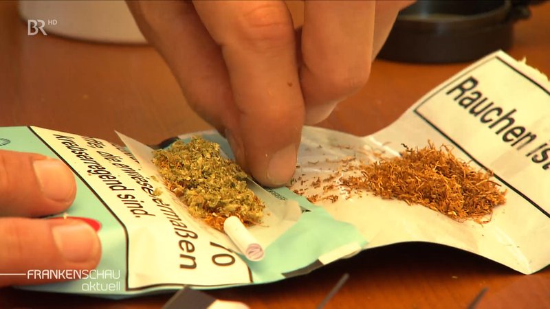 Eine linke Hand in Großaufnahme legt Cannabis und Tabak in ein Zigaretten-Papier