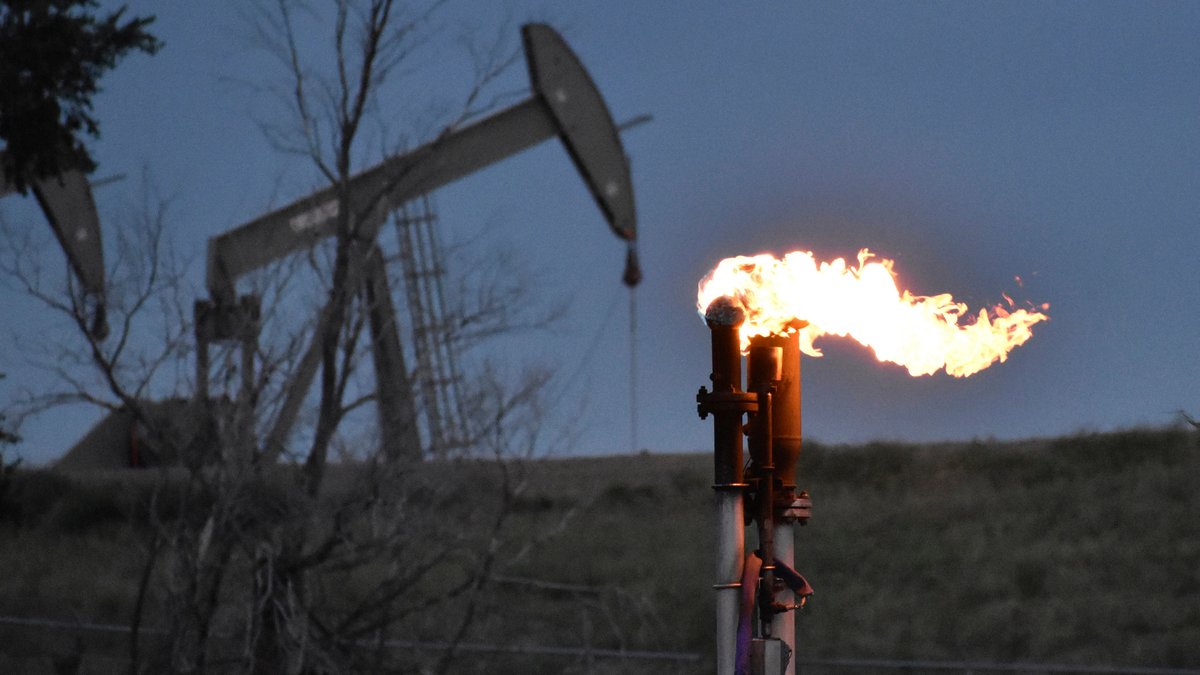 Eine Fackel zur Verbrennung von Methan aus der Ölförderung in Watford City, USA. Im Hintergrund eine Erdölpumpe.