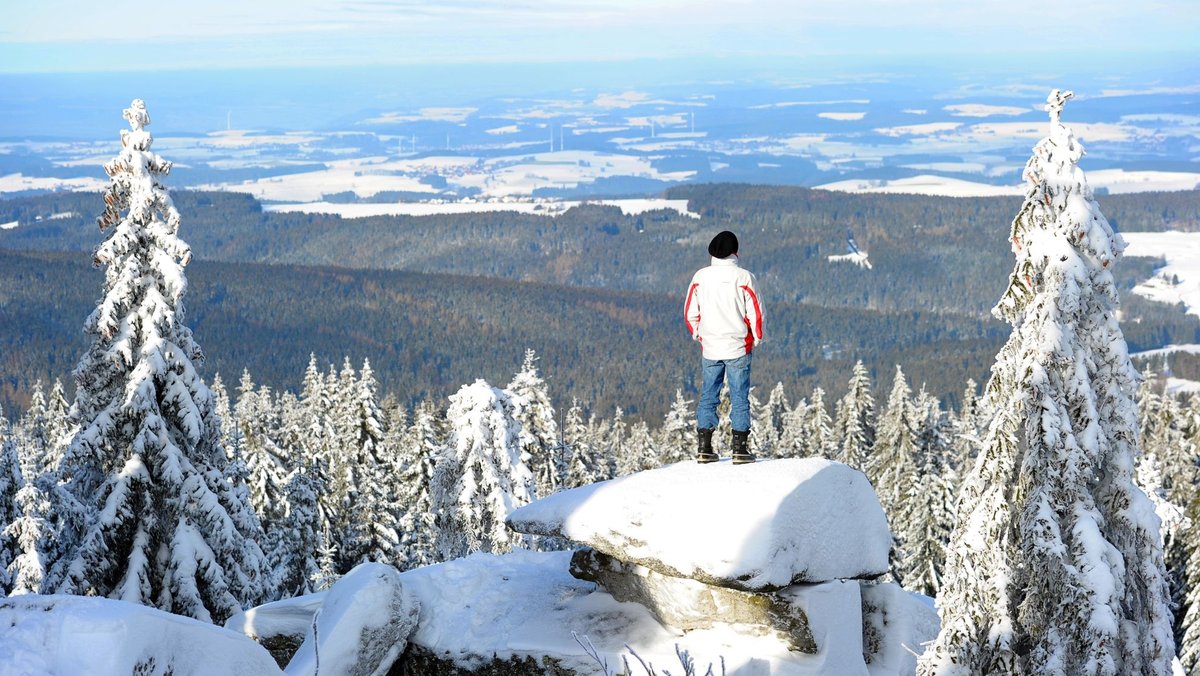 Eine Person steht auf einem Felsen und schaut in die verschneite Fichtelgebirgs-Landschaft. 
