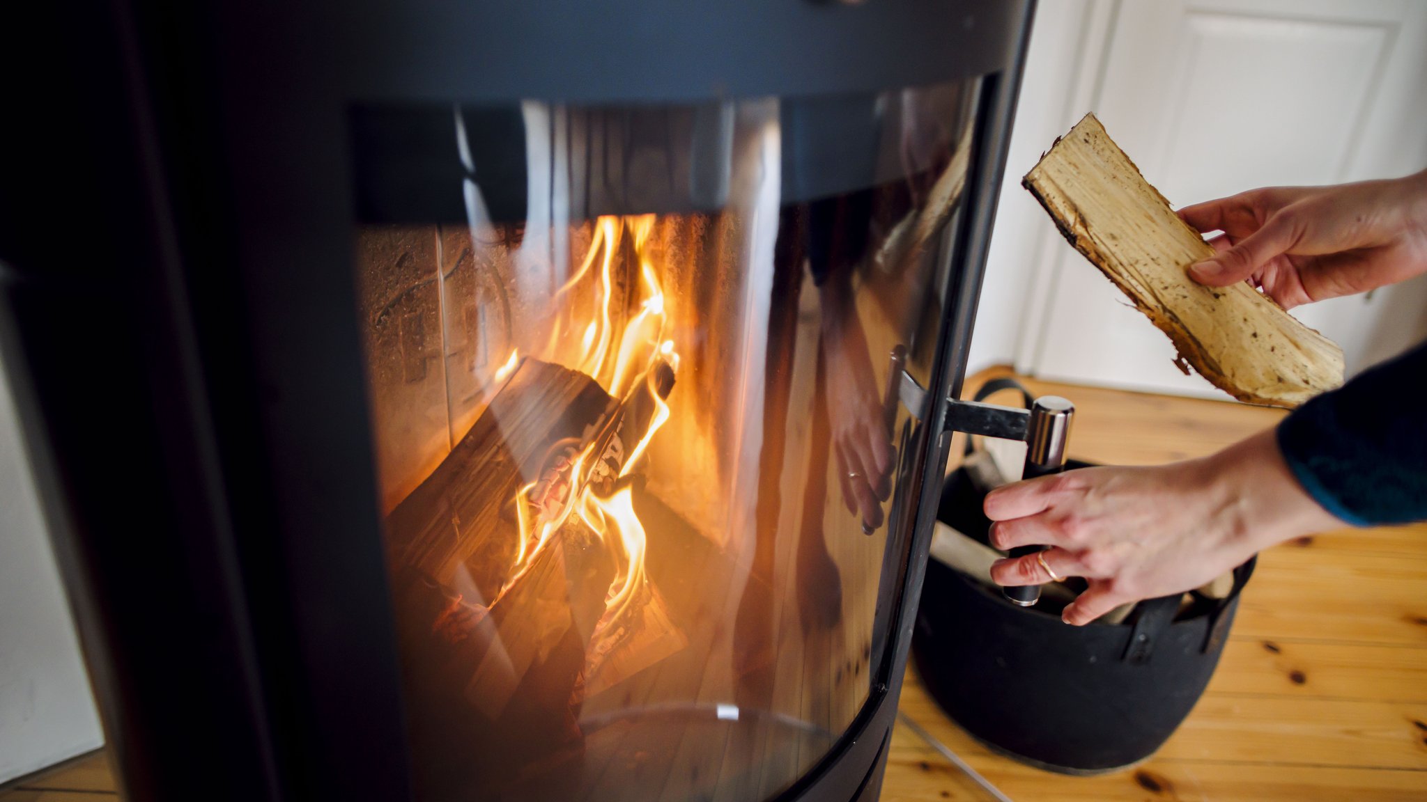 Symbolfoto: Eine Frau wirft ein Holzscheit in einen Kaminofen.