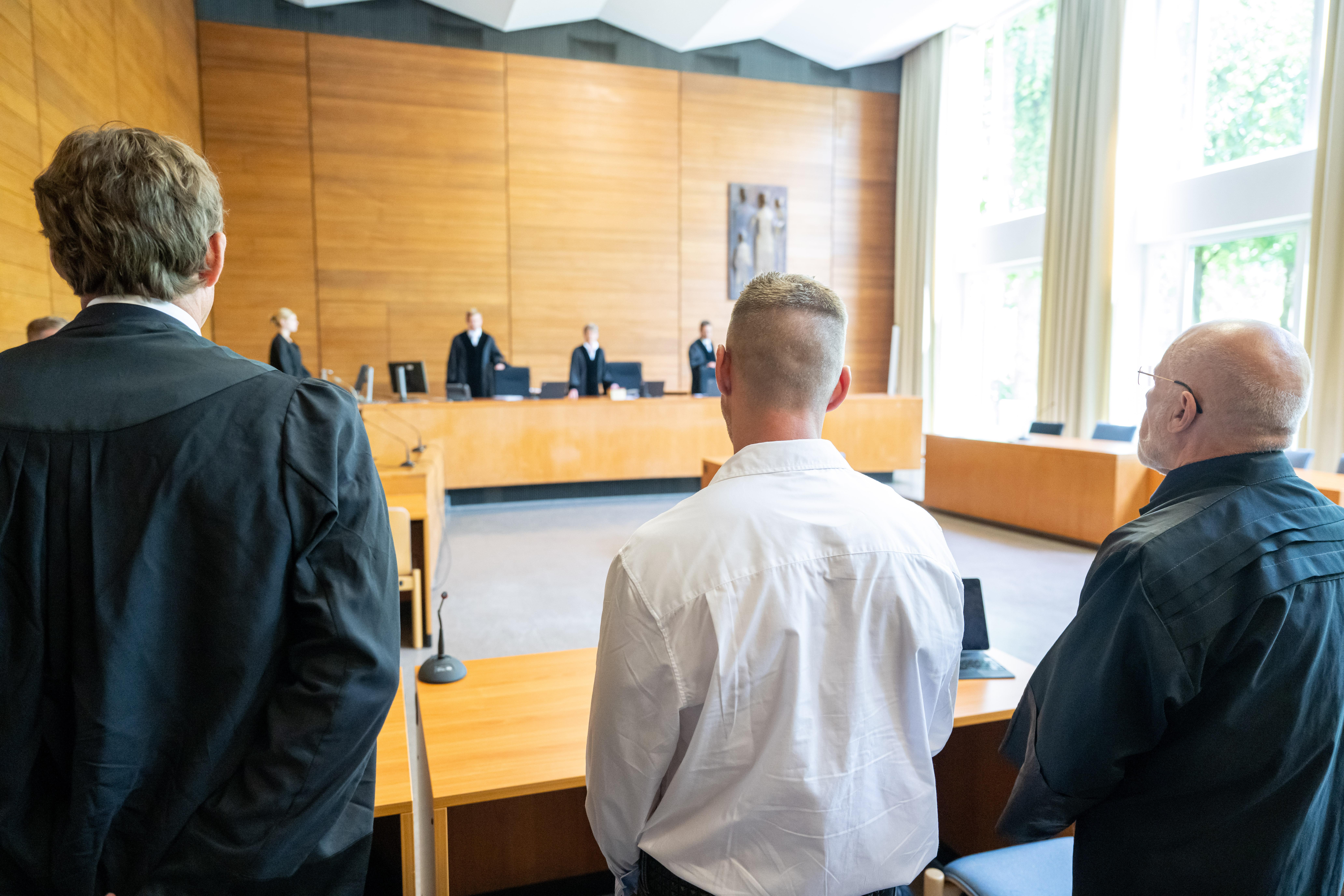 Der Kläger Andreas Perr (M) und seine Anwälte Andreas Schulz (r) und Markus Goldbach (l) stehen zu Prozessbeginn an ihren Plätzen im Gerichtssaal des Landgerichts Traunstein. 