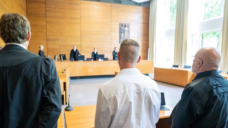 Der Kläger Andreas Perr (M) und seine Anwälte Andreas Schulz (r) und Markus Goldbach (l) stehen zu Prozessbeginn an ihren Plätzen im Gerichtssaal des Landgerichts Traunstein. 