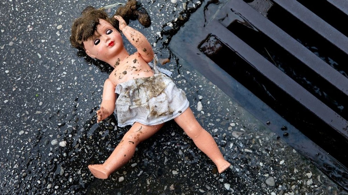 Eine Puppe liegt auf der nassen Straße neben einem Gulli.